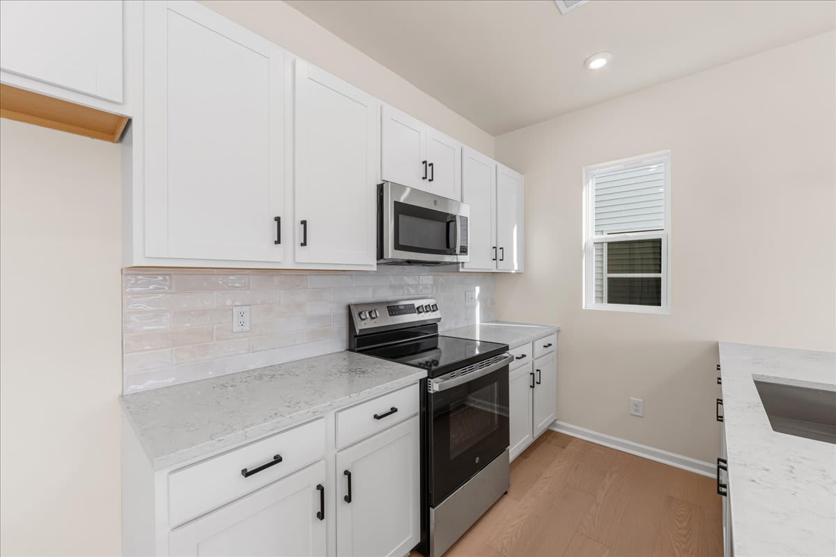 A modern, well-equipped kitchen with white cabinets, stainless steel appliances, and a tiled backsplash, set against a bright and airy background.