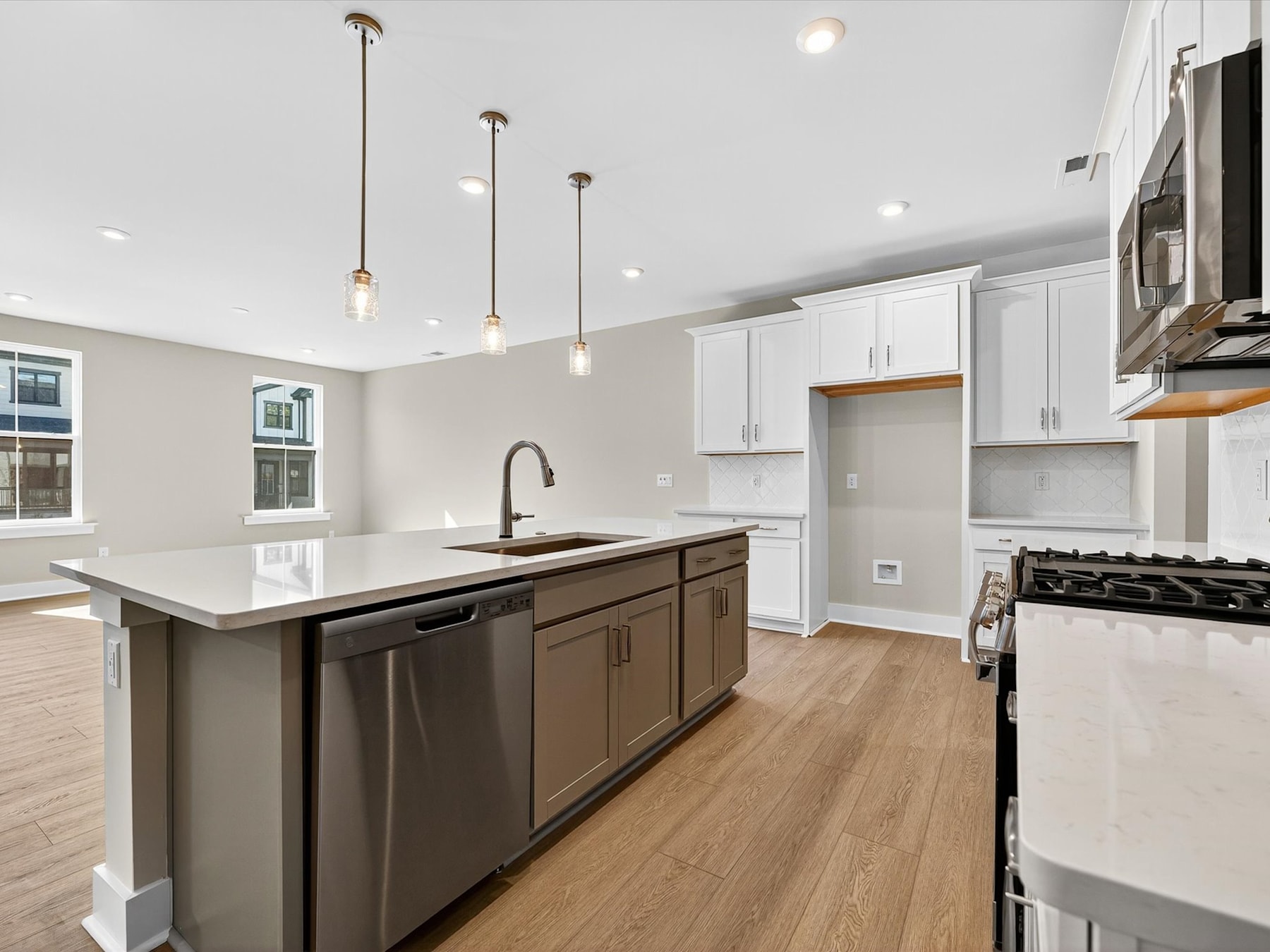 A modern, well-lit kitchen with white cabinets, dark wood island, and stainless steel appliances, set against a hardwood floor.