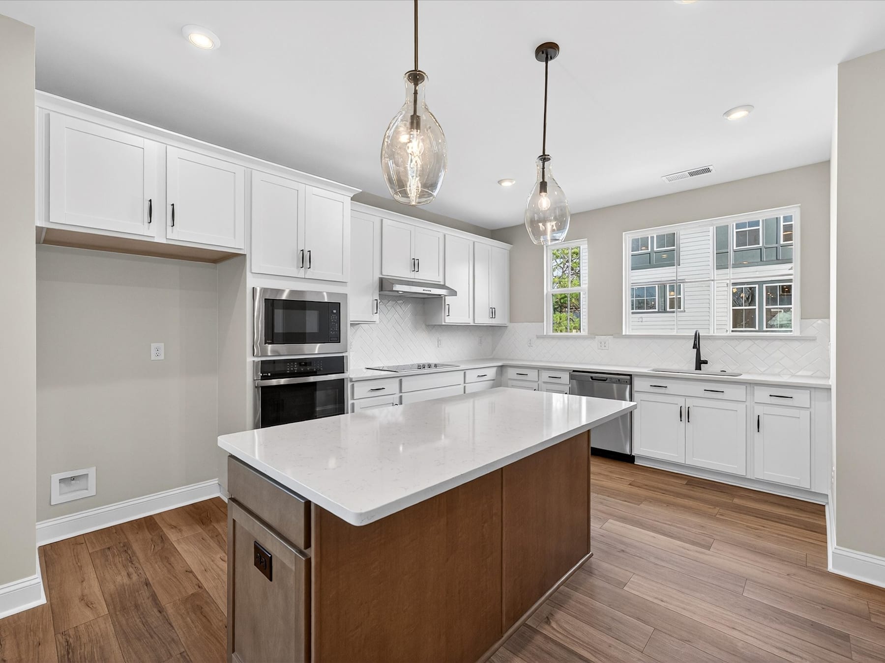 A modern, well-lit kitchen with white cabinets, wooden floors, and a central island with a marble countertop.