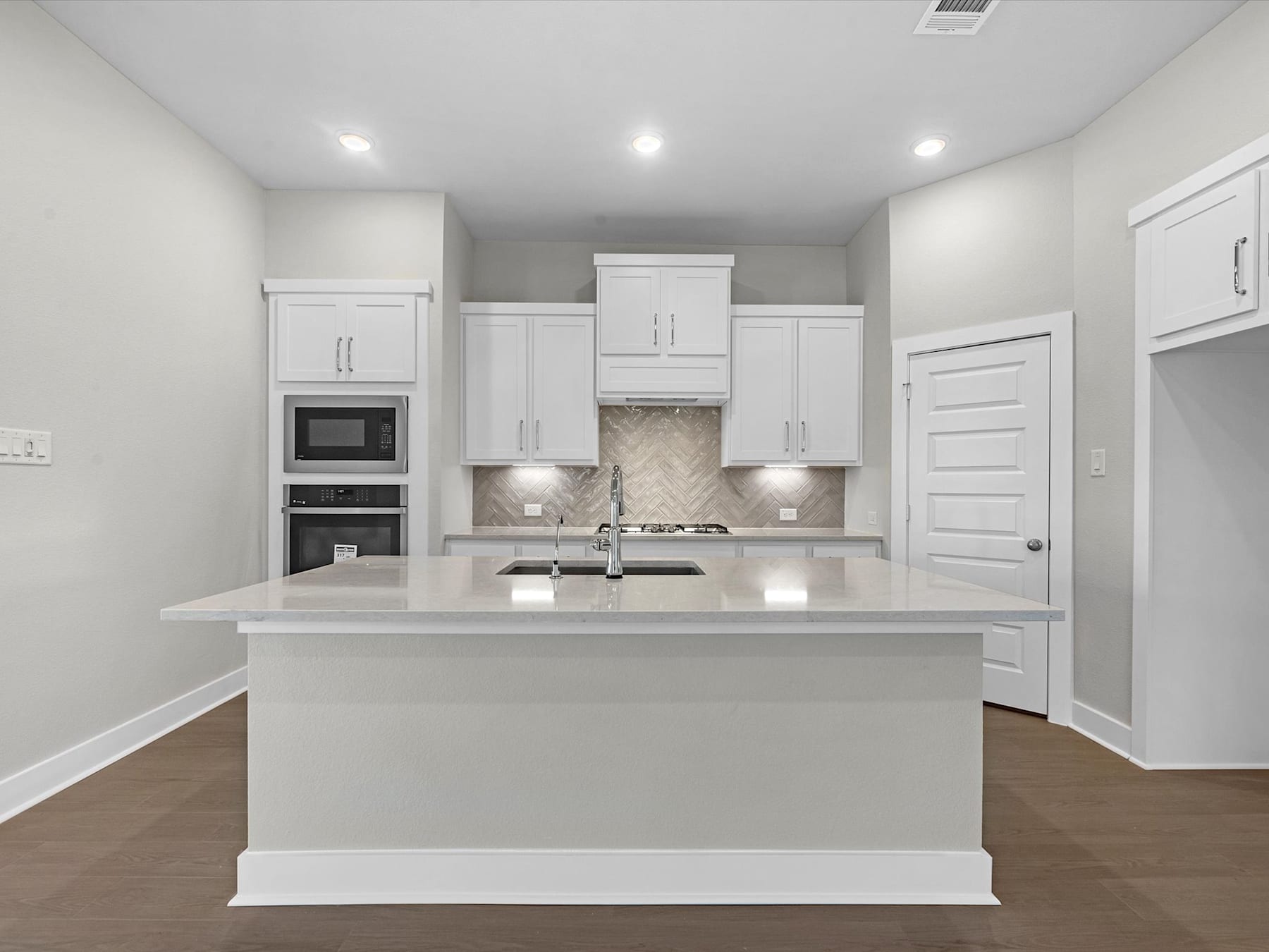 A modern, bright kitchen with white cabinets, a large island, and hardwood floors.