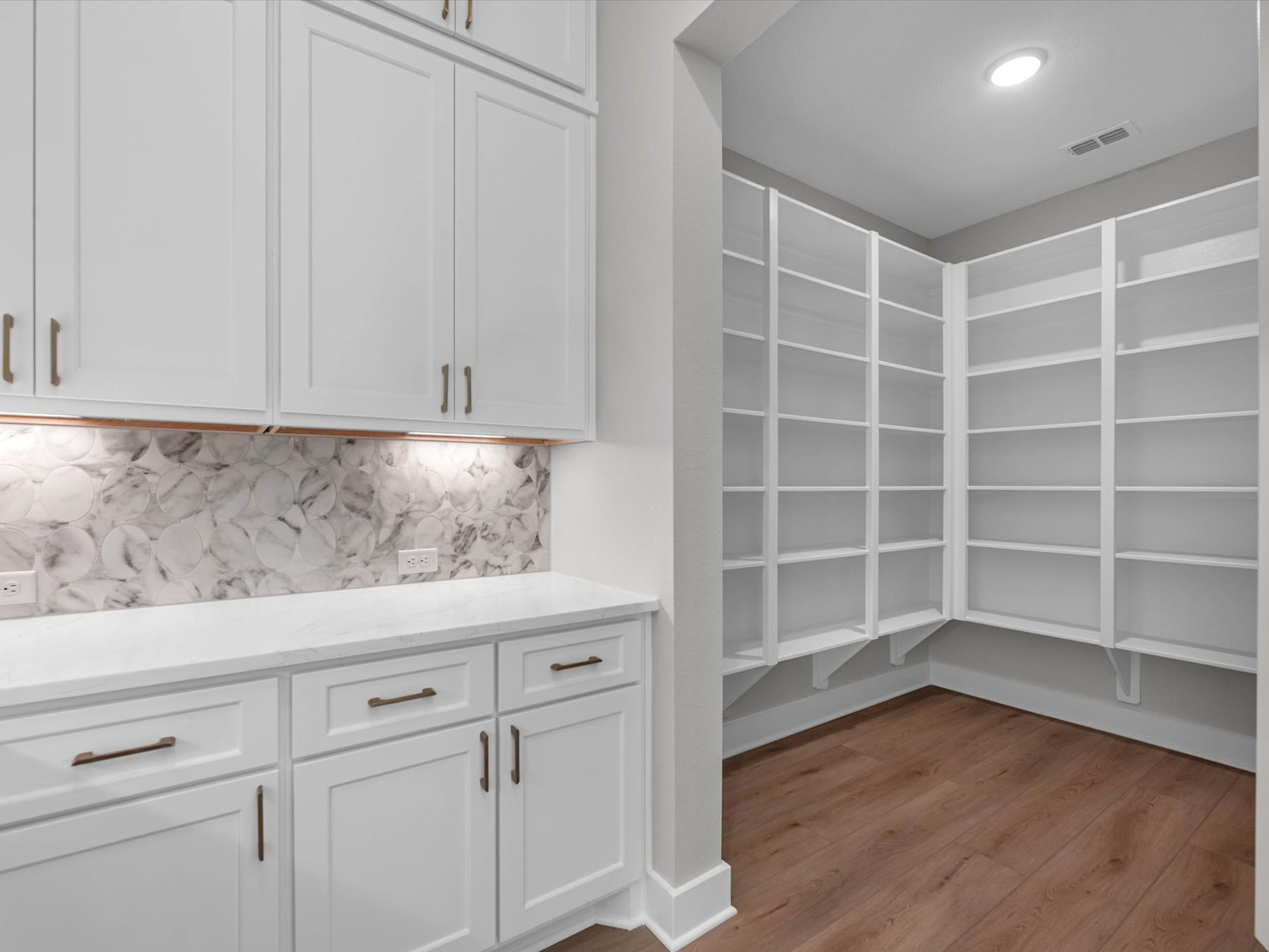 A spacious and well-organized walk-in closet with white cabinetry, a marble backsplash, and hardwood flooring.