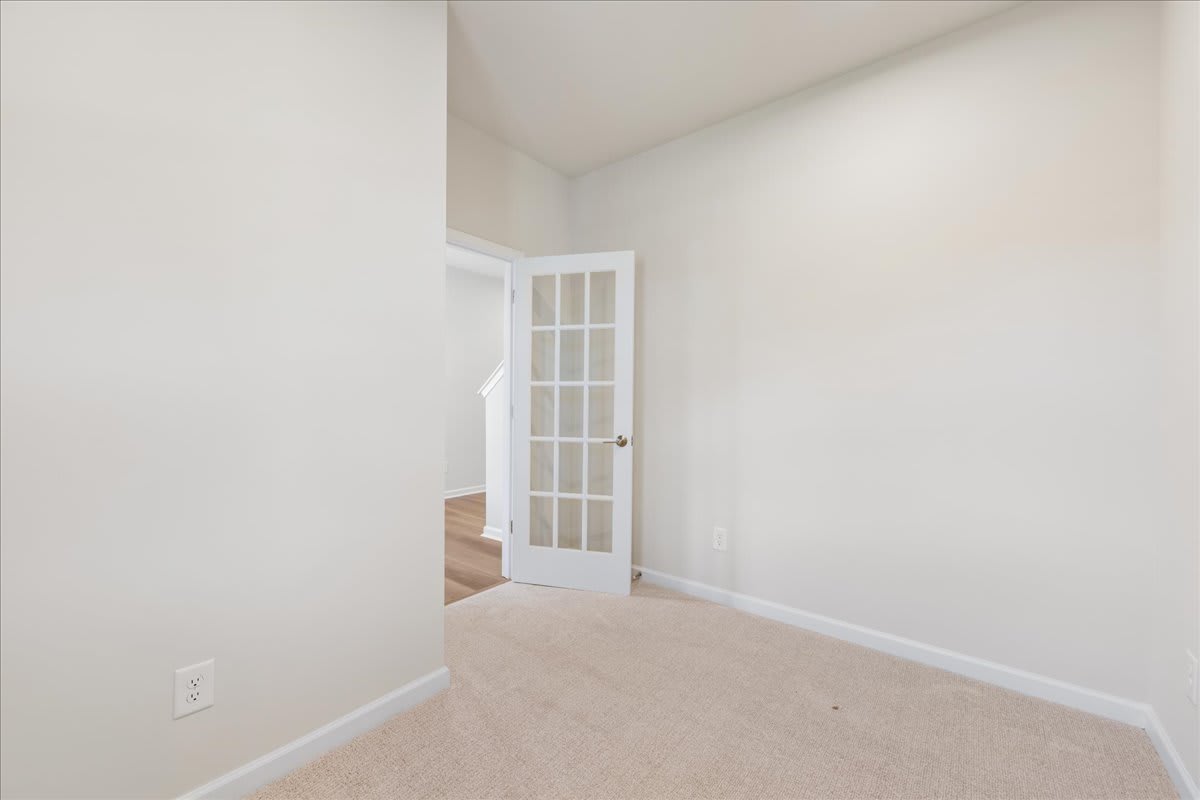 A white door with glass panes stands open in a bright, minimalist room with light-colored walls and floors.