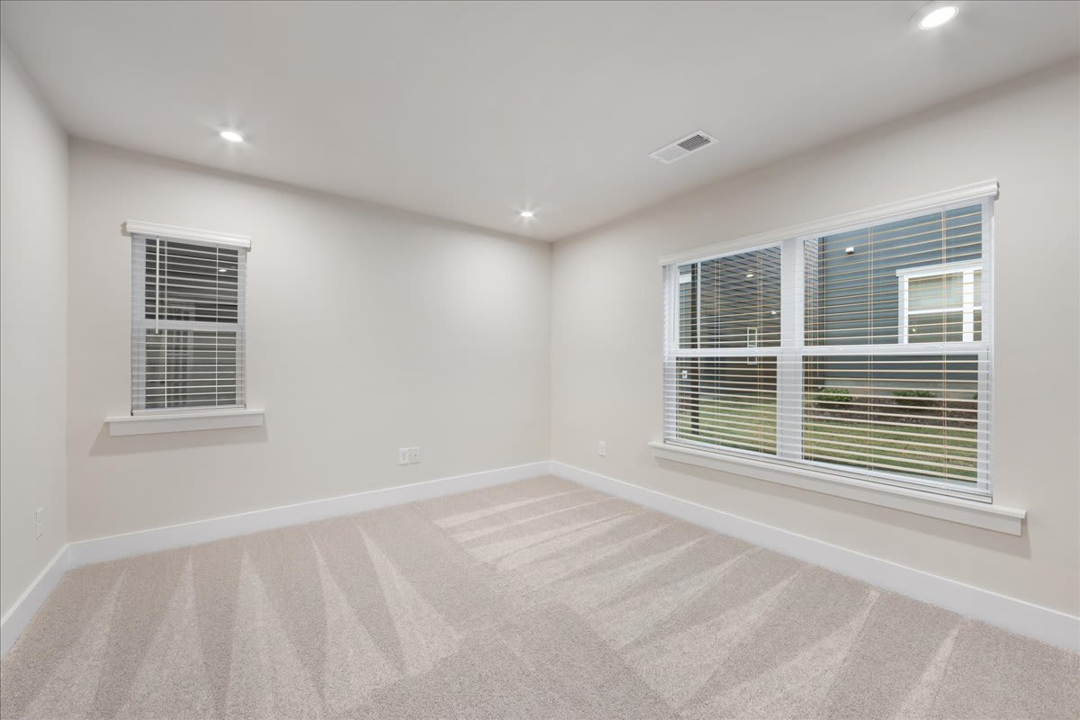 A spacious, well-lit room with white walls, hardwood floors, and large windows with horizontal blinds, creating a clean and minimalist atmosphere.