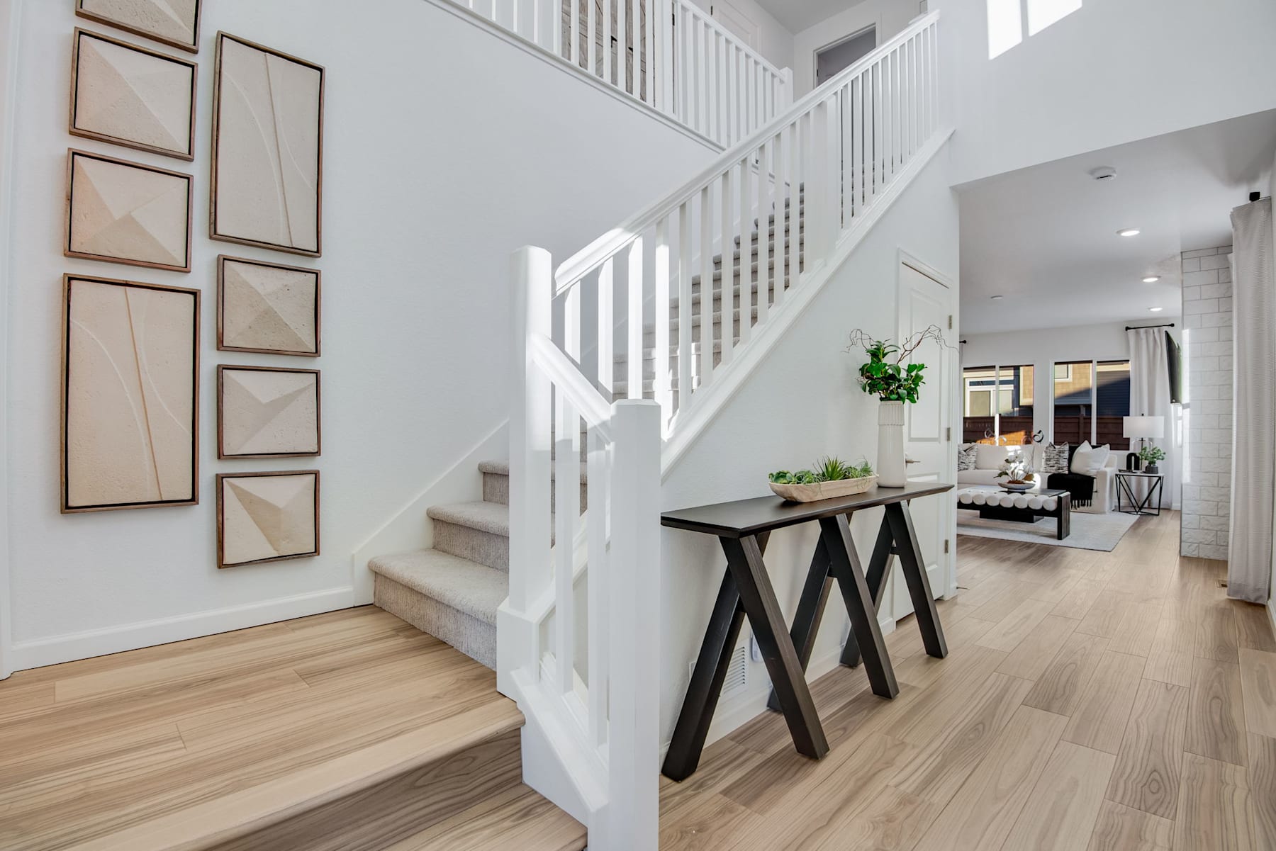 A modern, minimalist entryway with a wooden staircase, framed artwork on the walls, and a wooden console table in the foreground.