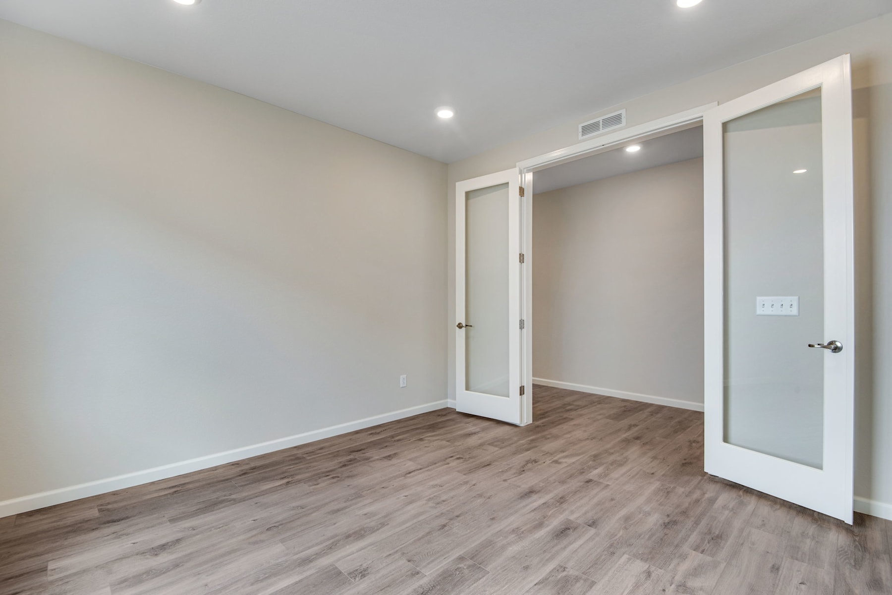 An empty room with white walls, a wooden floor, and a closet door with a glass panel.