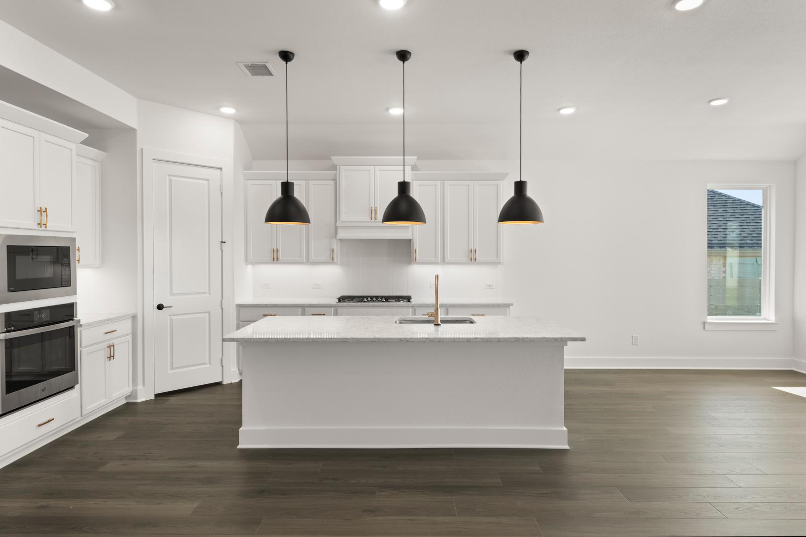 A modern, minimalist kitchen with a white island, dark pendant lights, and hardwood floors.