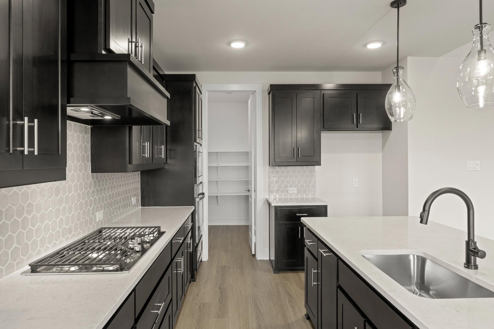 A modern, sleek kitchen with dark cabinets, a gas stove, and a sink with a faucet, set against a backdrop of white walls and a hardwood floor.