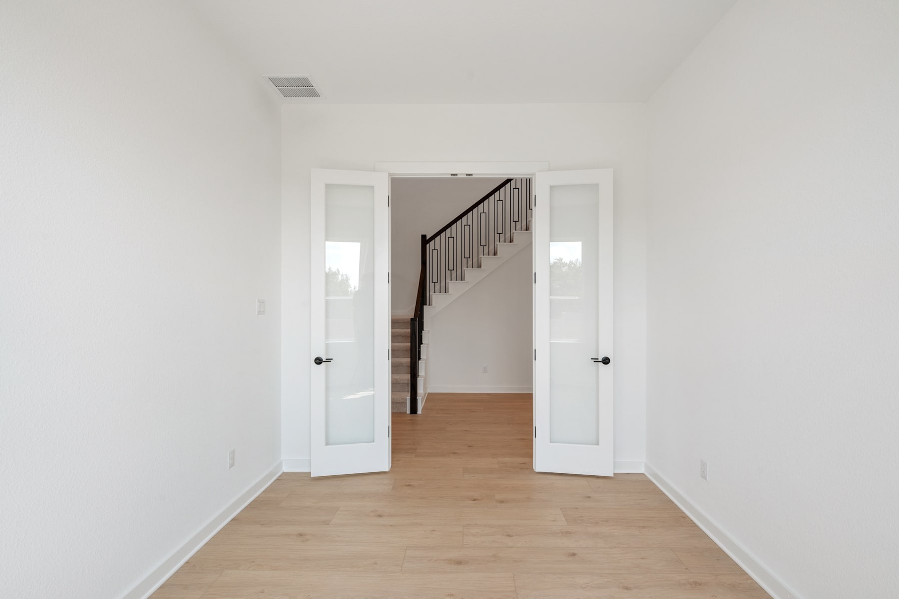 A bright, open hallway with white walls and a wooden floor leads to a staircase, with two closed doors visible on either side.