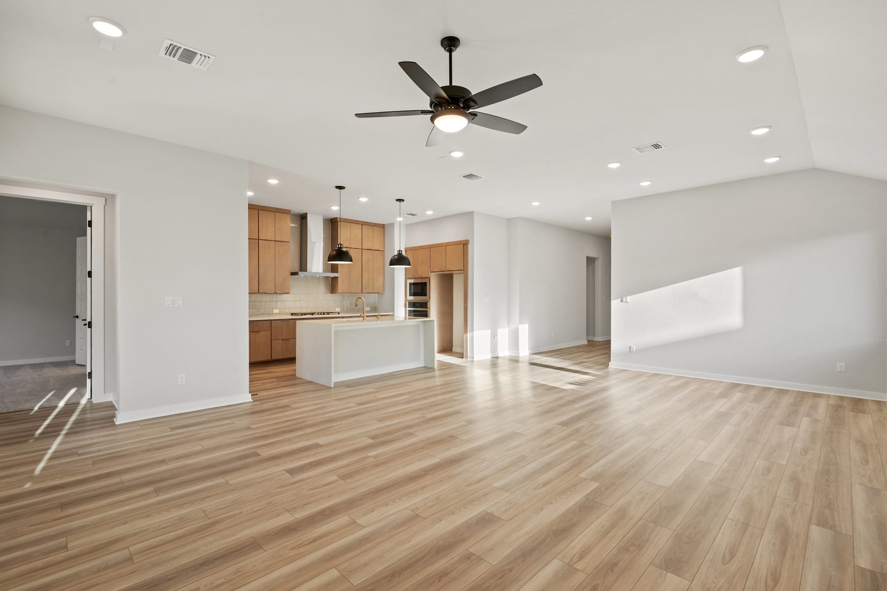 A spacious, open-concept living area with a modern kitchen, hardwood floors, and a ceiling fan, creating a bright and airy atmosphere.