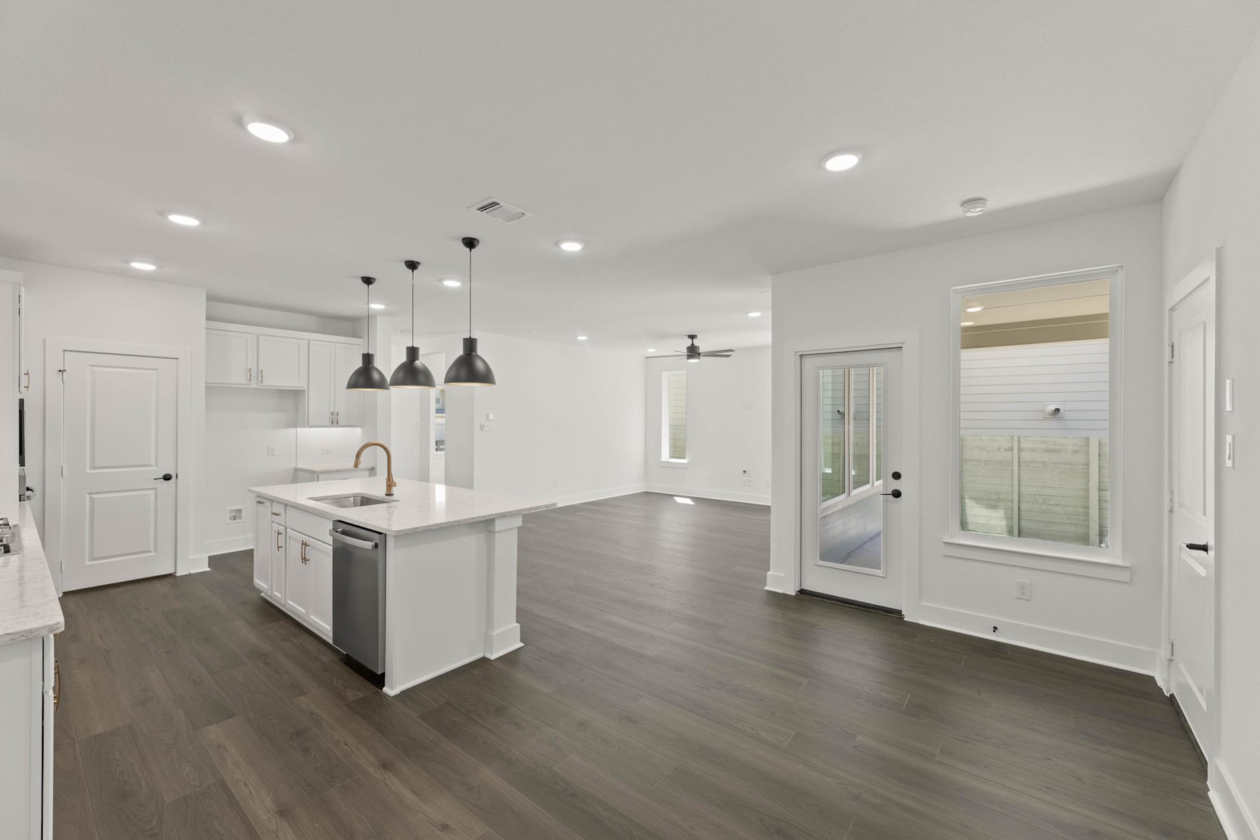 A modern, open-concept kitchen and living space with white walls, dark hardwood floors, and pendant lighting fixtures.