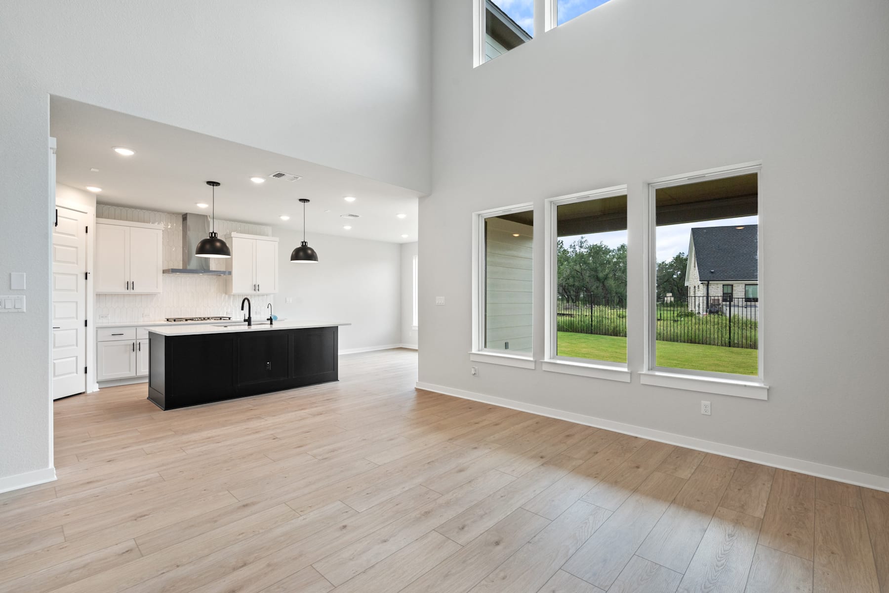 A spacious and modern open-concept kitchen and living room with large windows overlooking a grassy outdoor area.