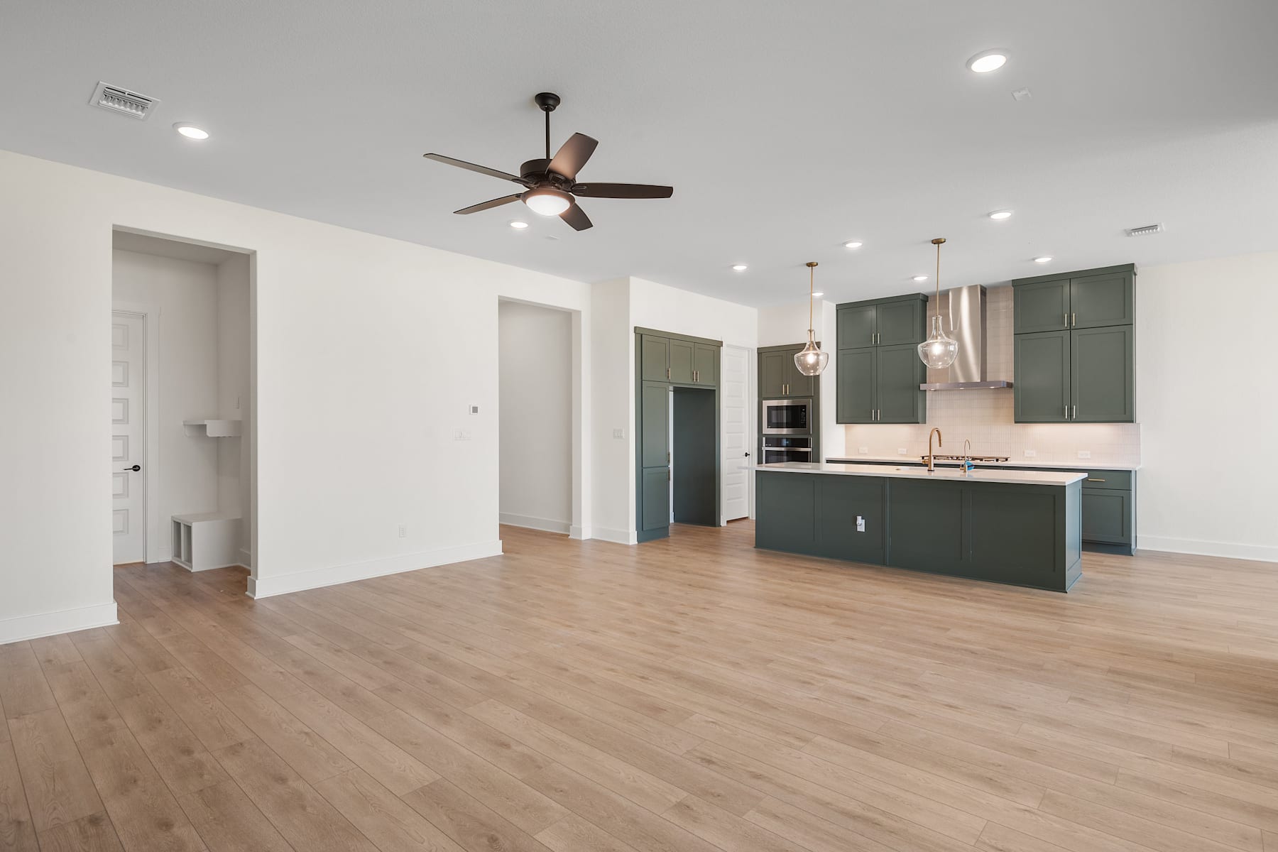 A modern, open-concept living space with a kitchen, hardwood floors, and a ceiling fan.