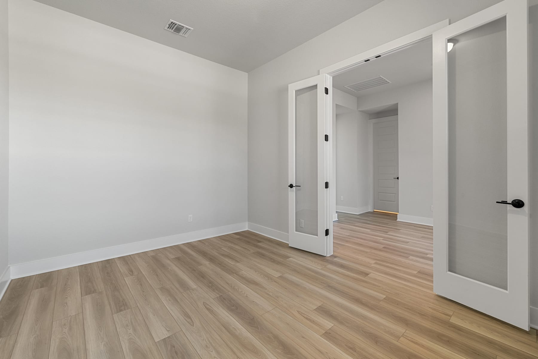 A spacious, minimalist room with white walls, wooden flooring, and a doorway leading to another area.