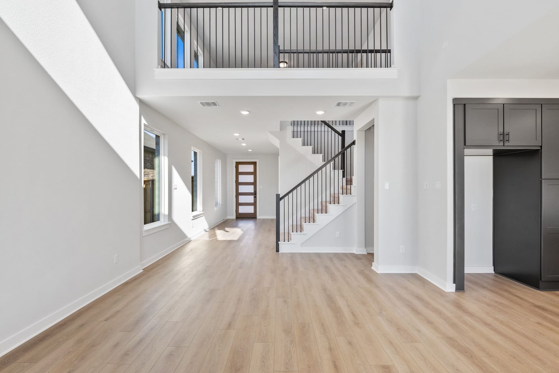 A bright and spacious interior with a wooden floor, a staircase, and a balcony visible in the background.