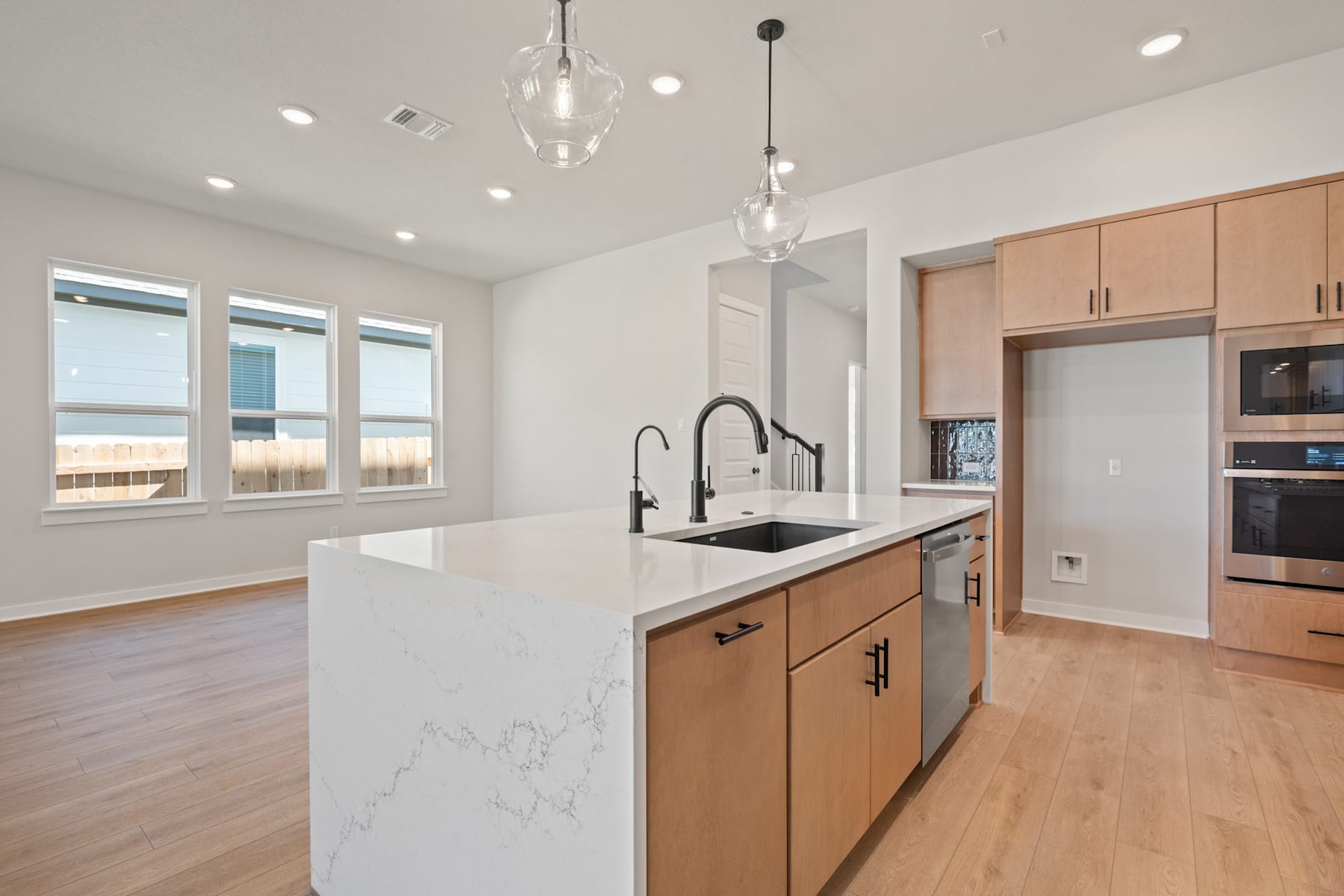 A modern and spacious kitchen with light-colored wood cabinets, a white marble countertop, and a large window providing natural light.