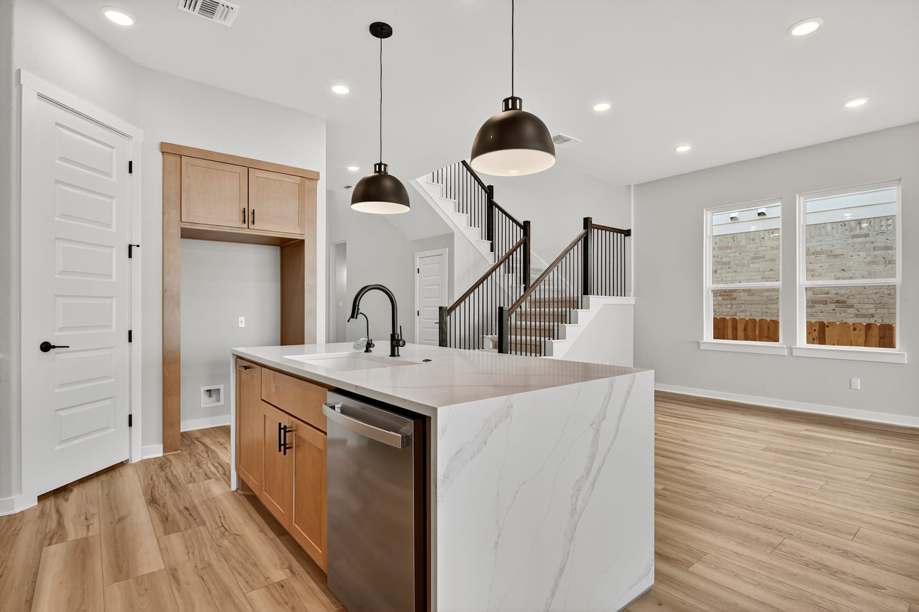A modern, open-concept kitchen and living space with light-colored wood floors, white walls, and pendant lighting fixtures.