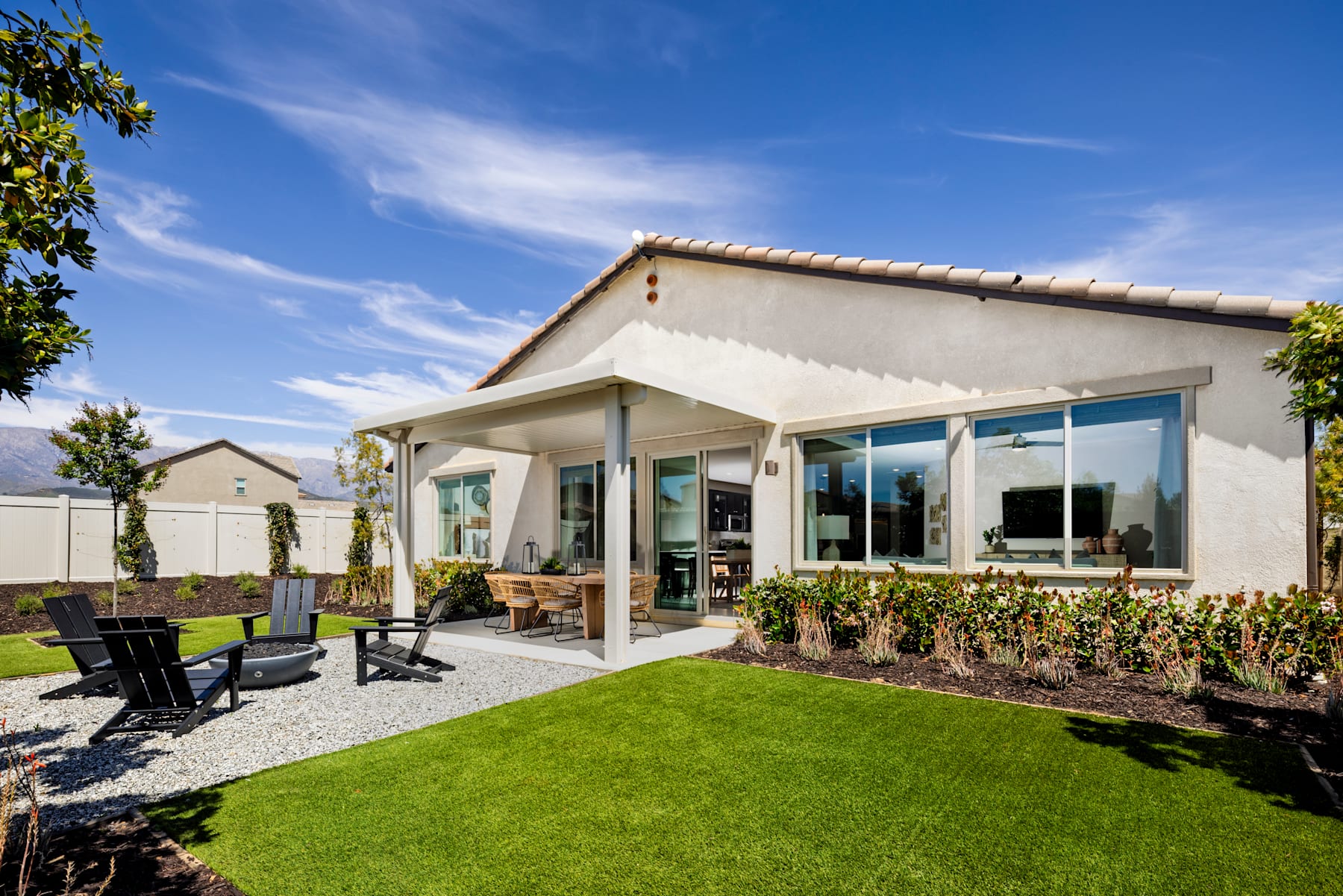 A modern, single-story house with a patio and a well-manicured lawn in the foreground, set against a clear blue sky with wispy clouds in the background.