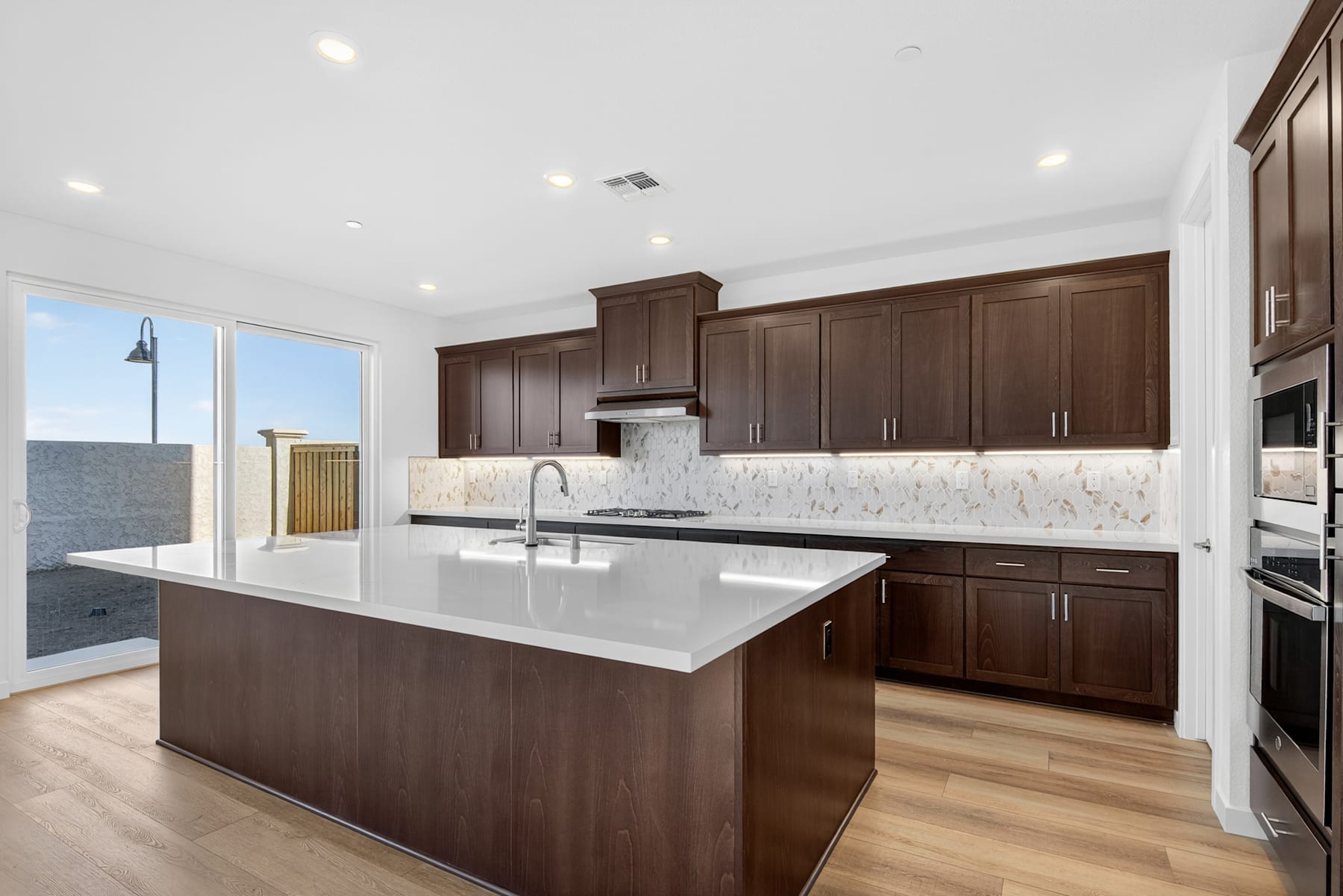 A modern, well-appointed kitchen with dark wood cabinetry, a large central island, and a bright, open layout with large windows providing ample natural light.