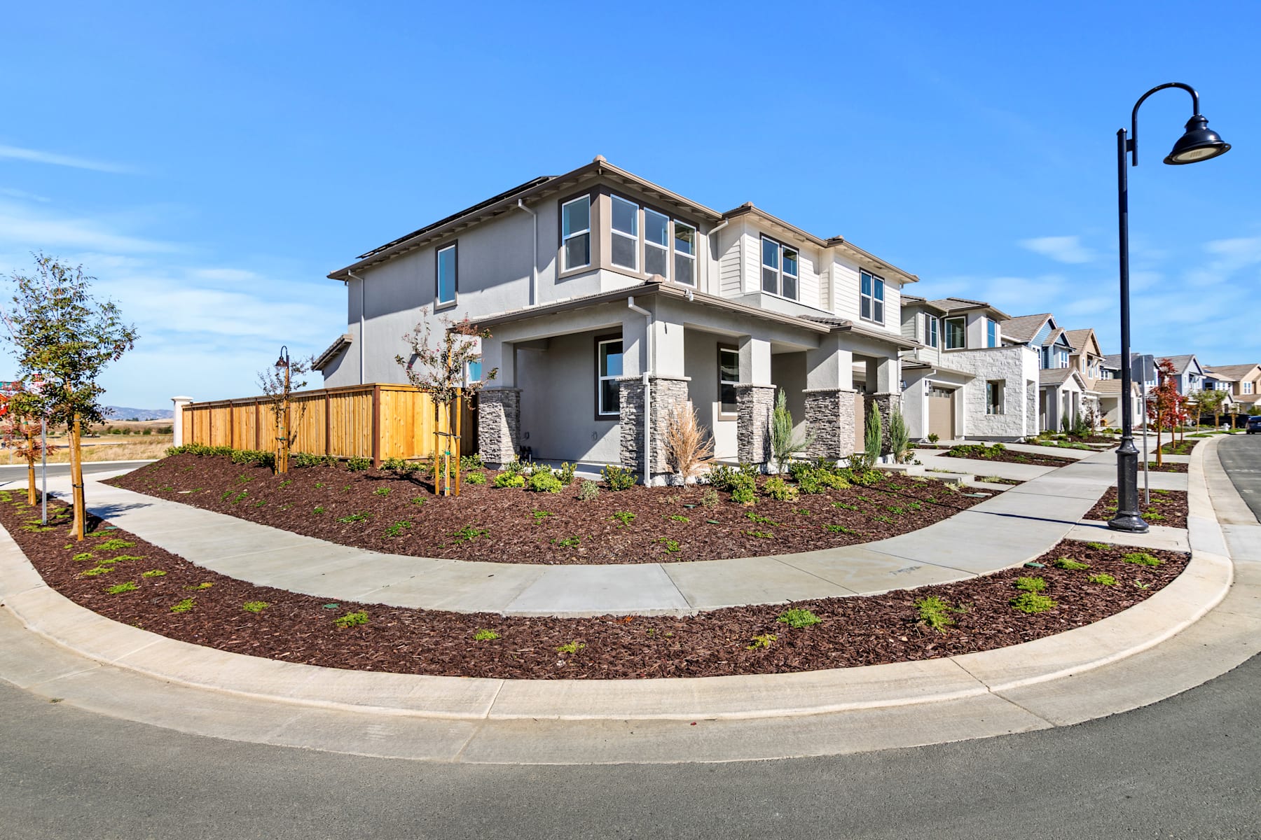 A modern, multi-story residential building with a well-landscaped front yard, surrounded by a paved driveway and a street lamp in the foreground.