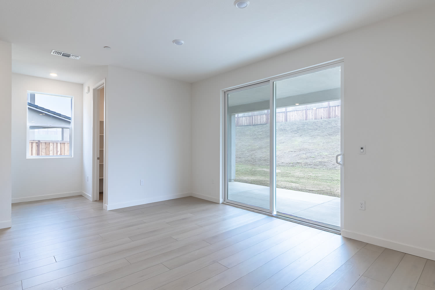 A spacious, well-lit room with a sliding glass door leading to an outdoor area, featuring a hardwood floor and a minimalist, modern design.