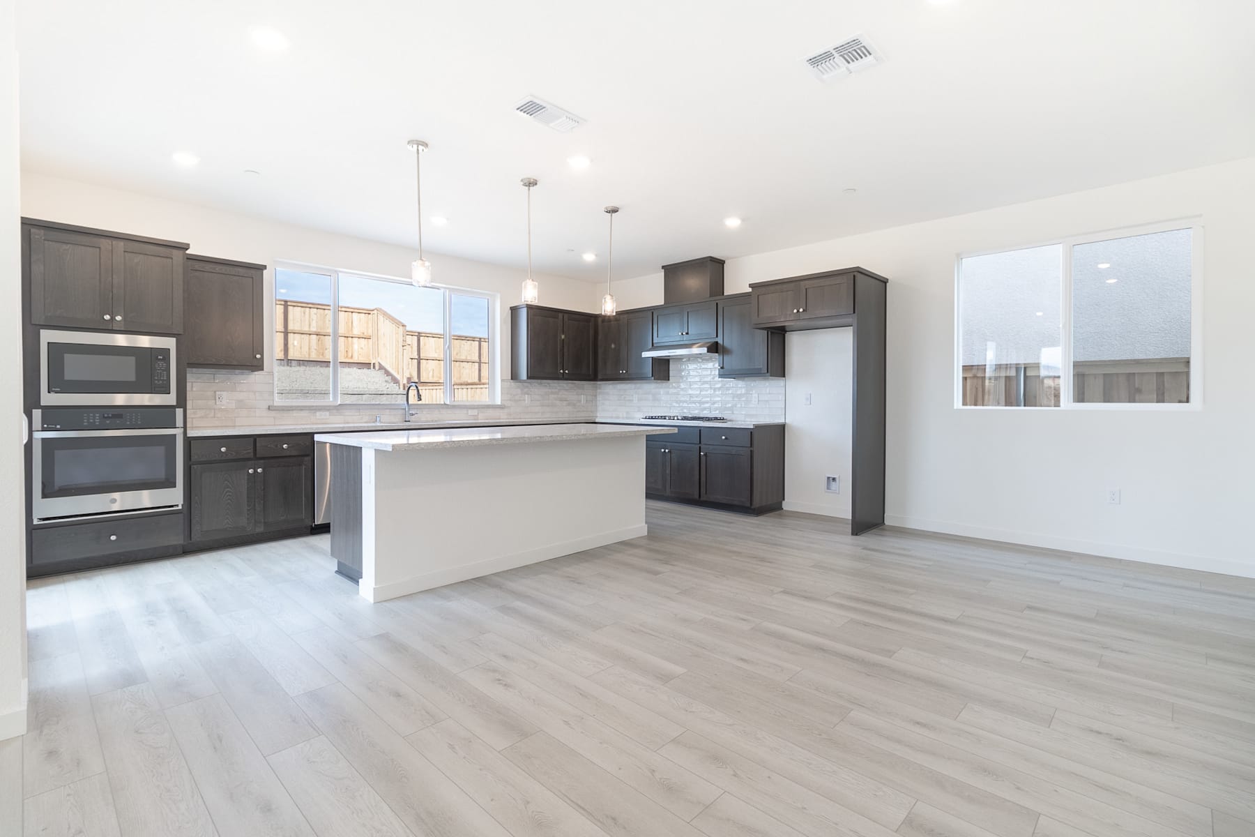 A modern, open-concept kitchen with dark cabinets, stainless steel appliances, and a large central island on a light-colored hardwood floor.