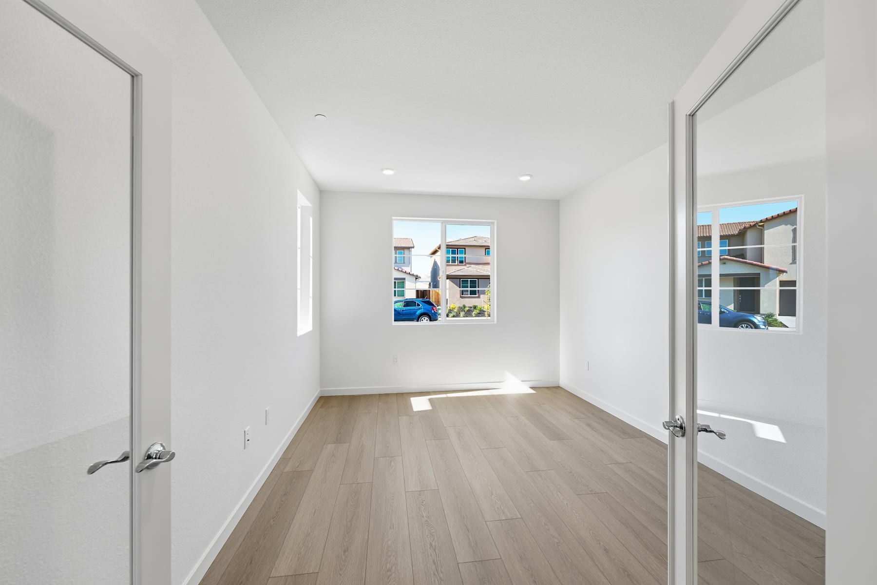 A bright, spacious room with white walls, hardwood floors, and a window providing natural light.