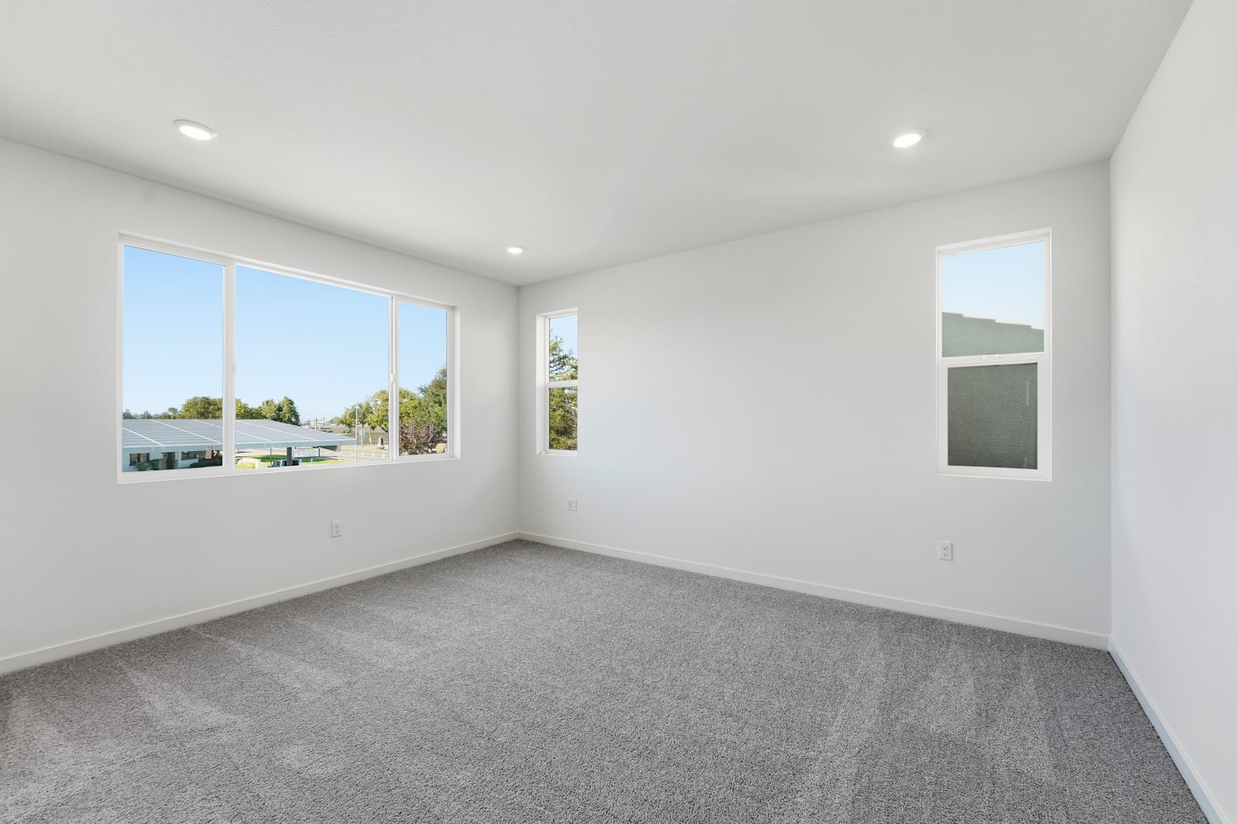 A bright, spacious room with large windows overlooking a scenic outdoor landscape, featuring a clean, minimalist design with gray carpeting and white walls.
