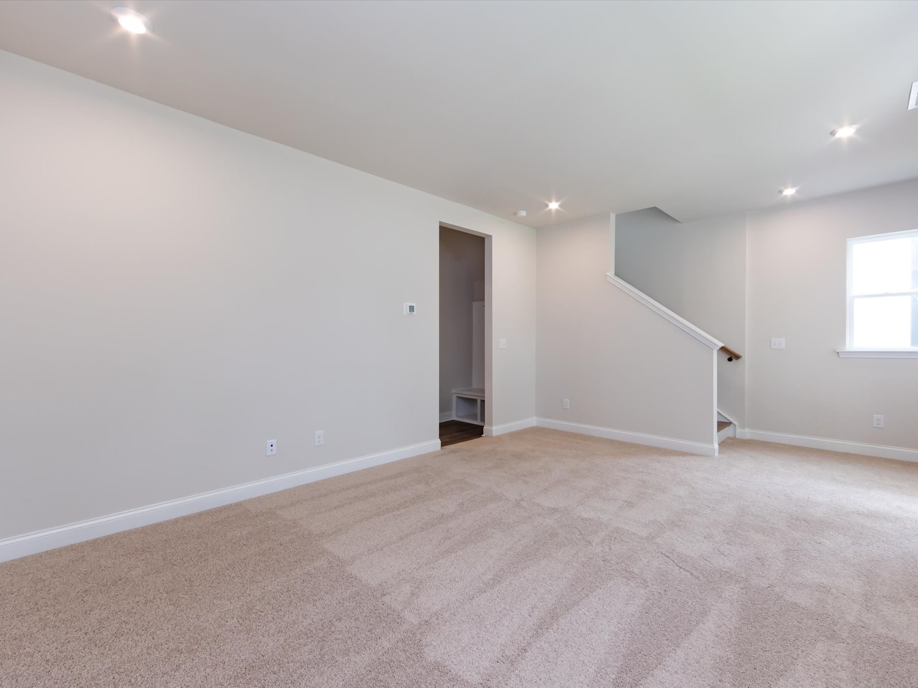 A spacious, well-lit room with light-colored walls, a carpeted floor, and a doorway leading to another area.