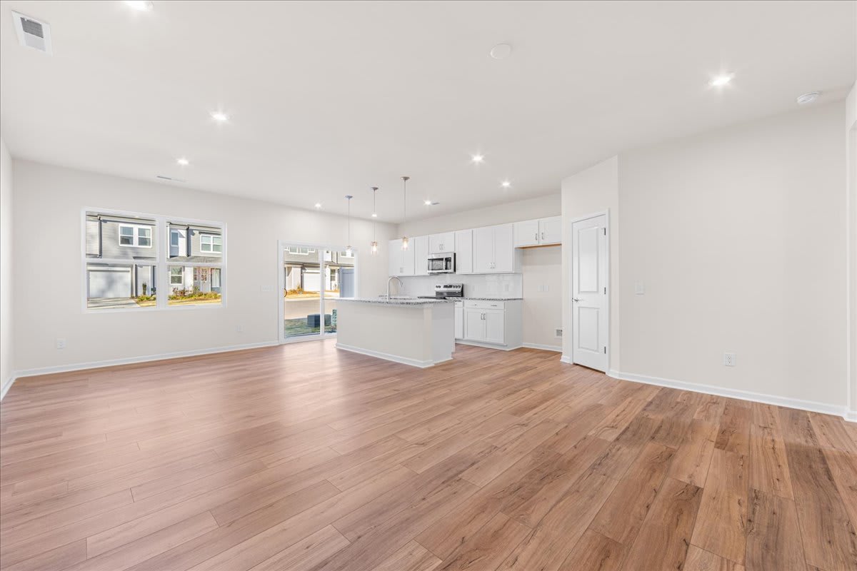 A spacious and bright open-concept kitchen and living room with white cabinets, hardwood floors, and large windows allowing natural light to fill the space.