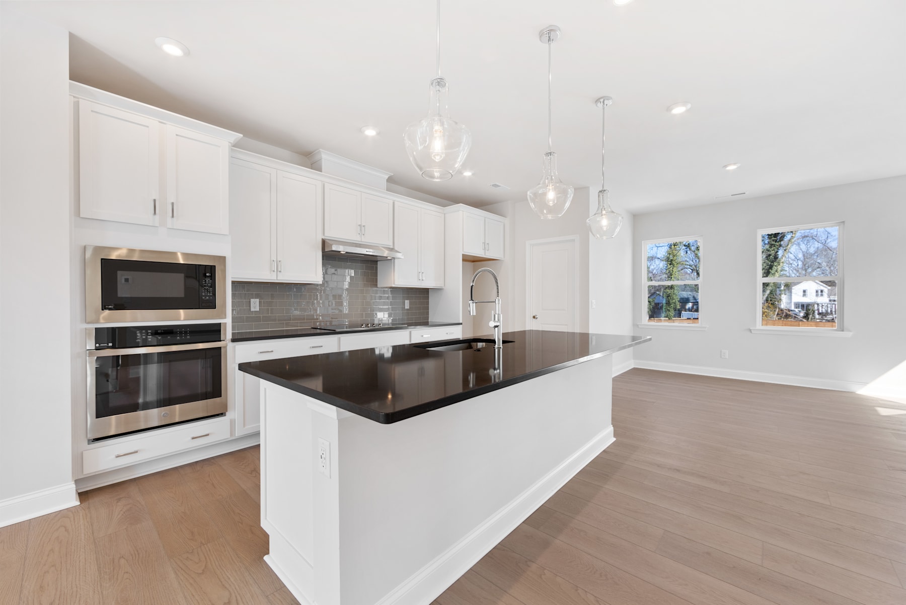 A modern, open-concept kitchen with white cabinets, stainless steel appliances, and a large island with a dark countertop, set against a bright and airy backdrop.