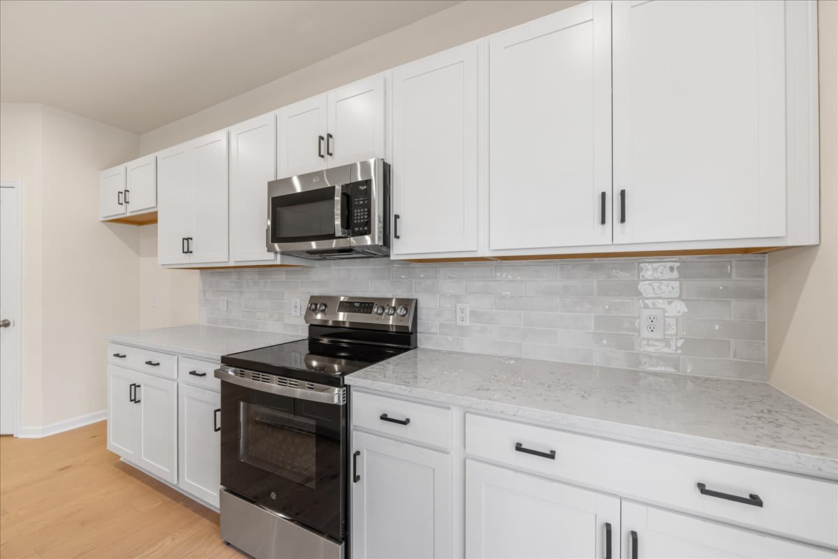 A modern kitchen with white cabinets, a stainless steel oven, and a microwave mounted above the stove, set against a tiled backsplash and hardwood floors.