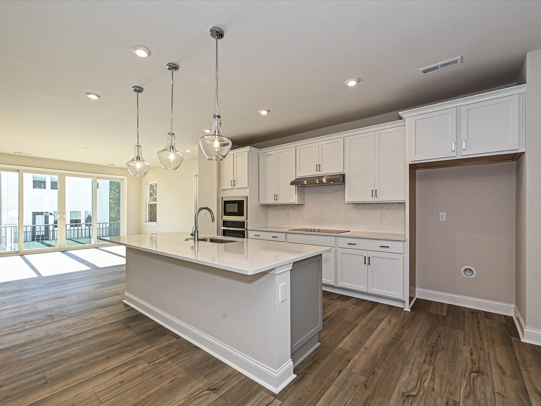 A modern, open-concept kitchen with white cabinets, a large island, and pendant lighting, leading into a living area with hardwood floors.