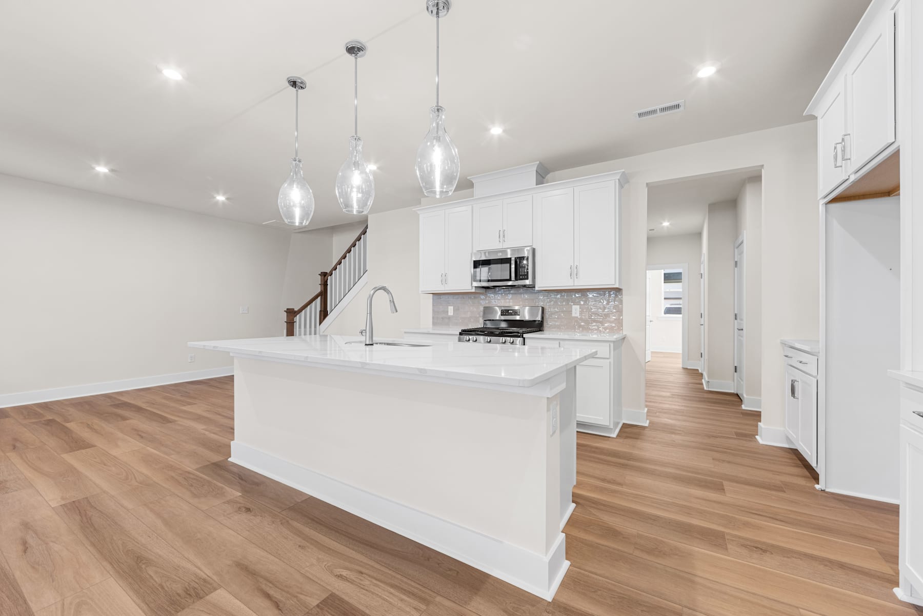 A modern, open-concept kitchen with white cabinets, a large island, and pendant lighting fixtures, set against a backdrop of hardwood floors and a neutral color scheme.