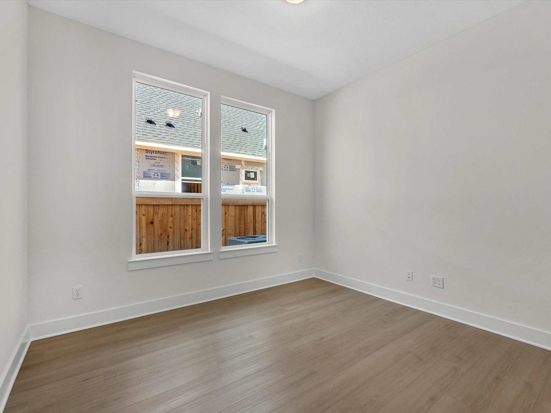 A spacious, well-lit room with wooden flooring and large windows, providing a bright and airy atmosphere.