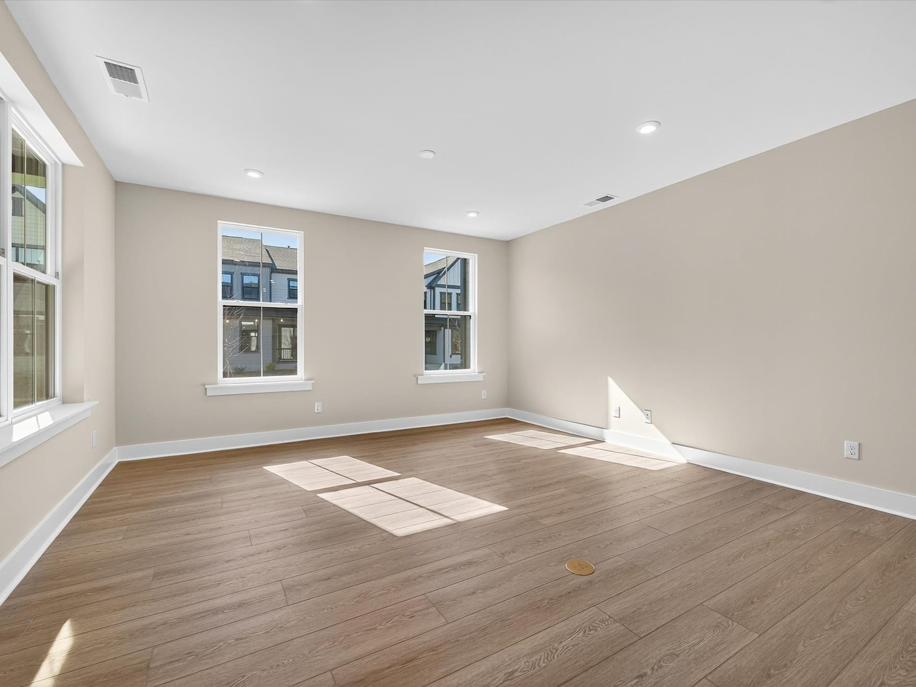 A spacious, well-lit room with hardwood floors, neutral-colored walls, and large windows providing natural light.