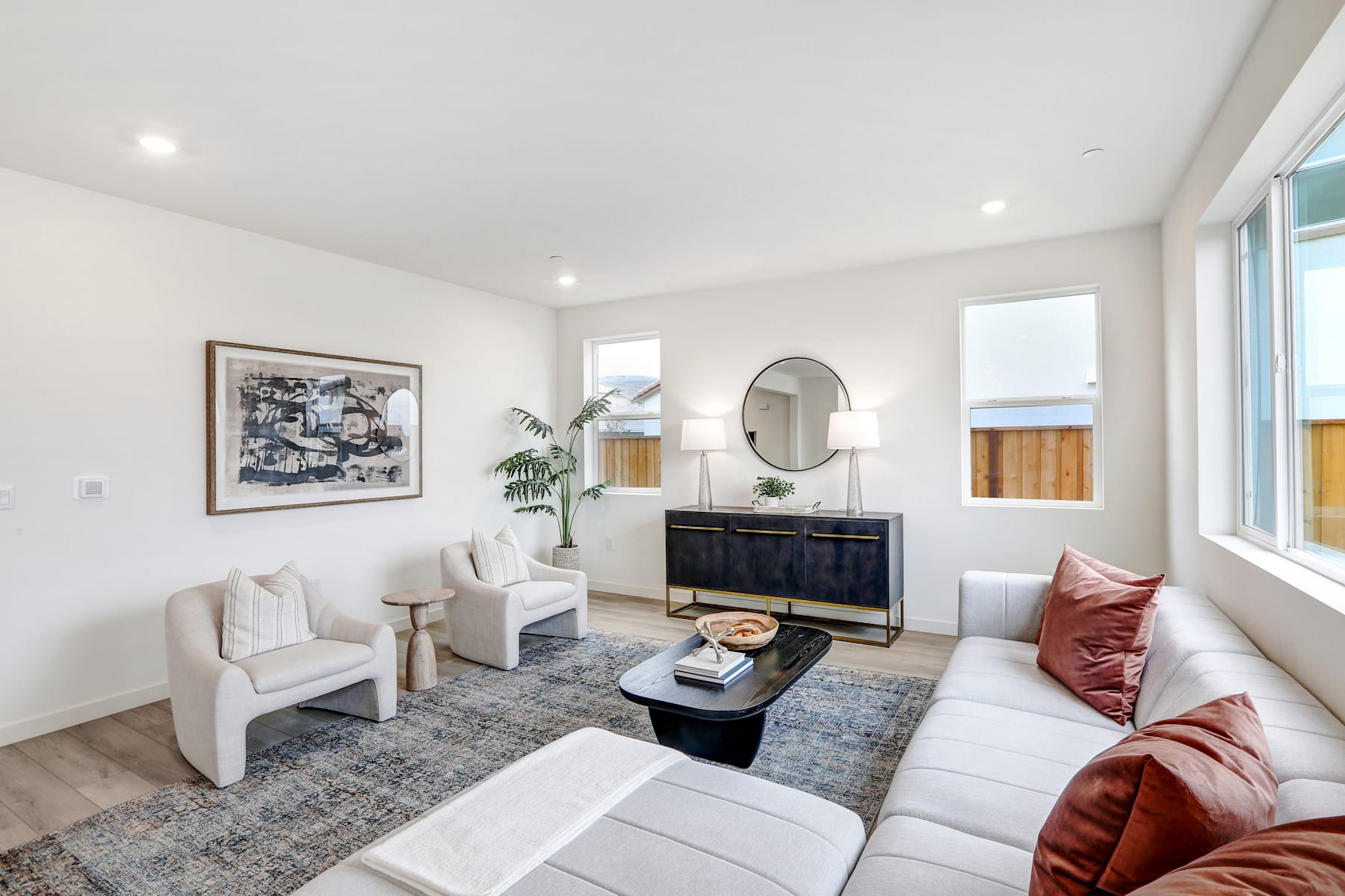 A modern and cozy living room with a white sofa, armchairs, a coffee table, and a decorative mirror on the wall.