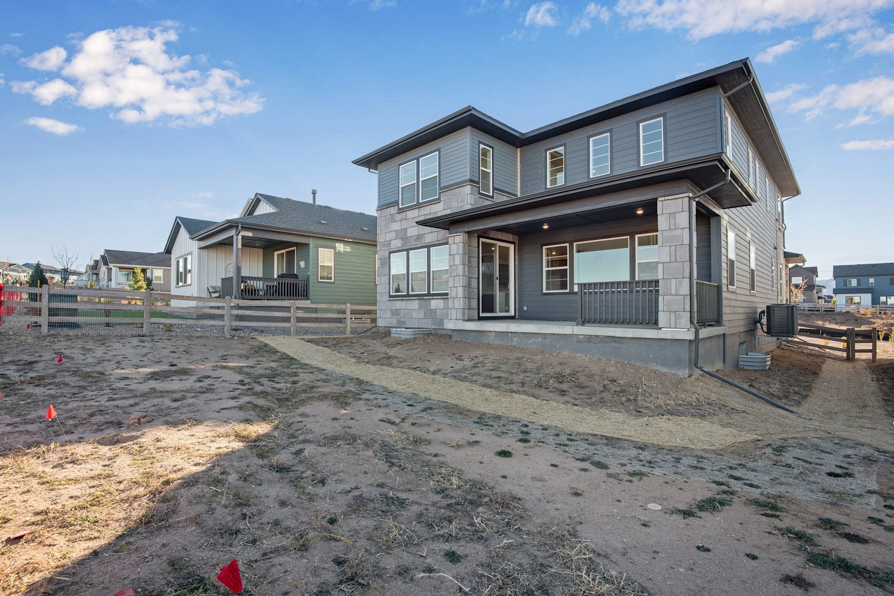 A newly constructed two-story residential building with a gray exterior and a paved driveway in the foreground, set against a backdrop of a partly cloudy sky.
