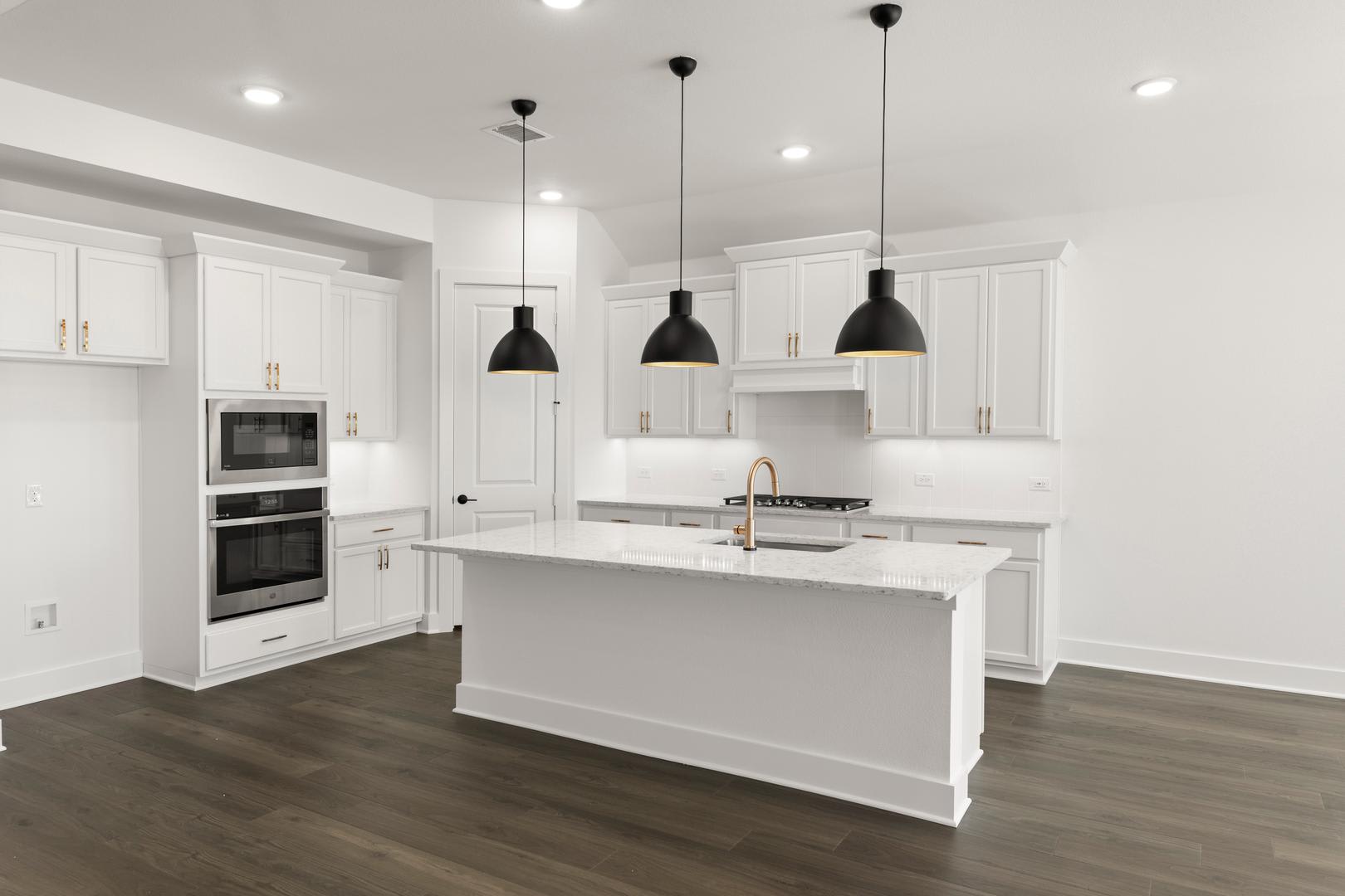 A modern, bright kitchen with white cabinets, a central island, and three black pendant lights hanging above.