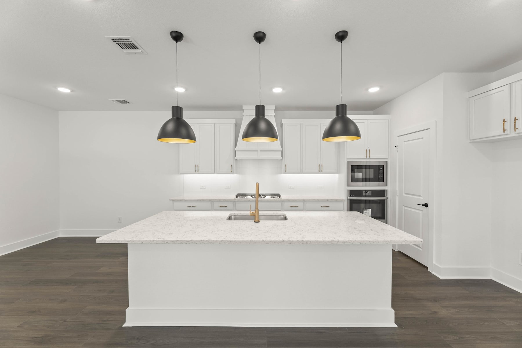 A modern, minimalist kitchen with a large white island, dark pendant lights, and stainless steel appliances.