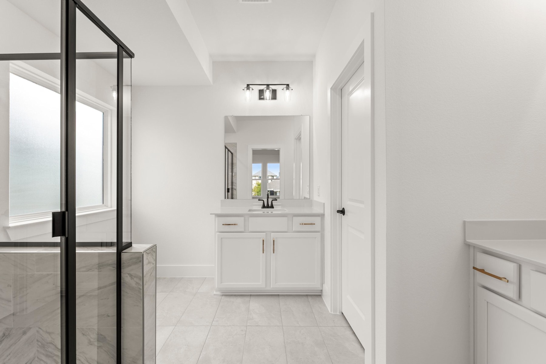 A bright, modern hallway with a white vanity cabinet and a glass-paneled door leading to another room.