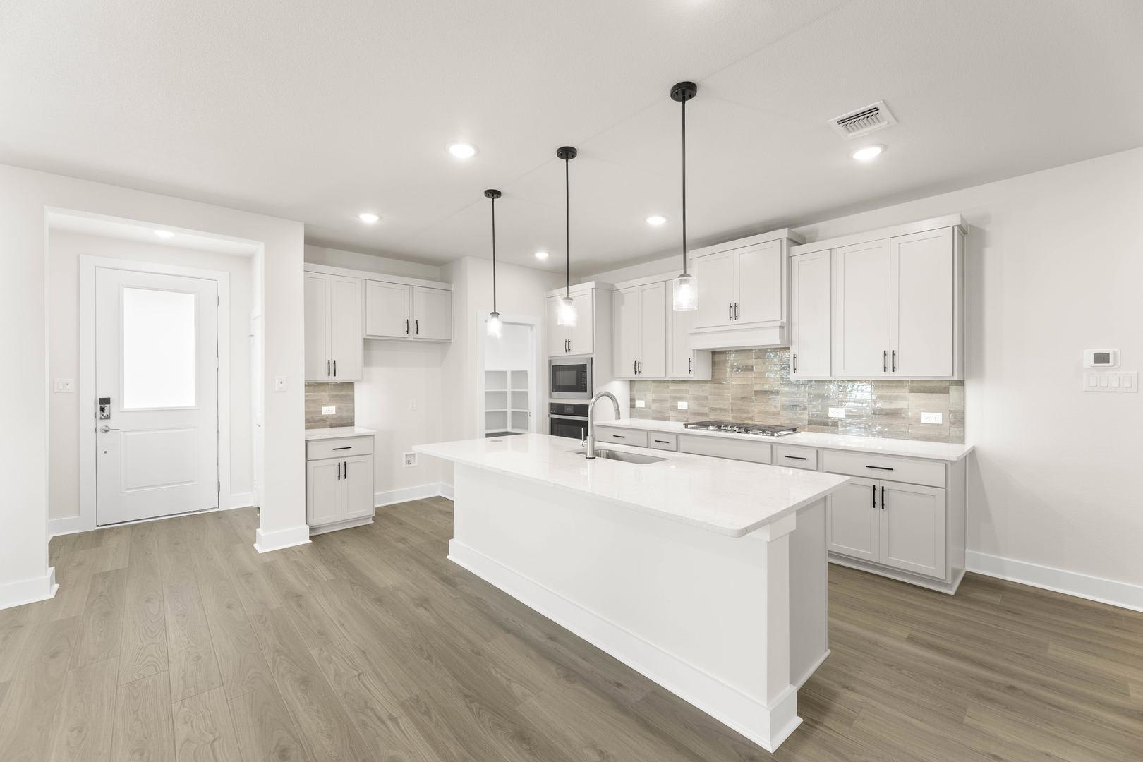 A modern, bright, and spacious kitchen with white cabinets, a large island, and pendant lighting fixtures.