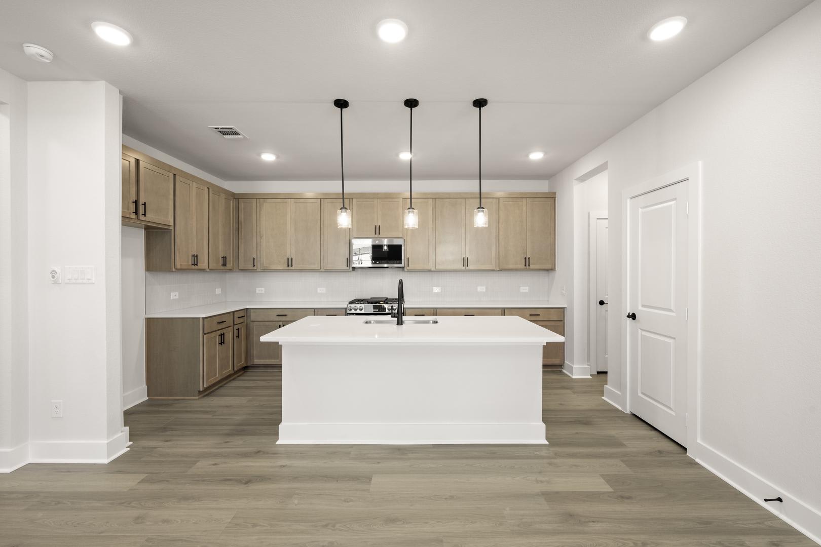 A modern, open-concept kitchen with light-colored wood cabinets, a white island, and pendant lighting fixtures.
