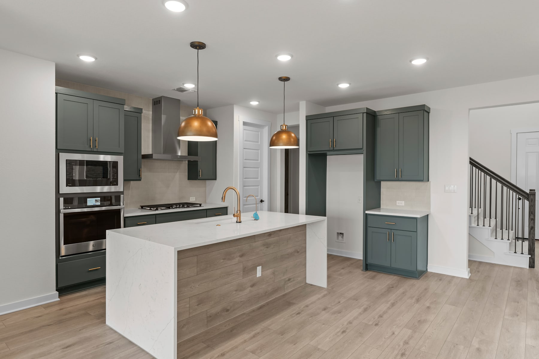 A modern and spacious kitchen with gray cabinets, white countertops, and wooden flooring, featuring pendant lights and a central island.