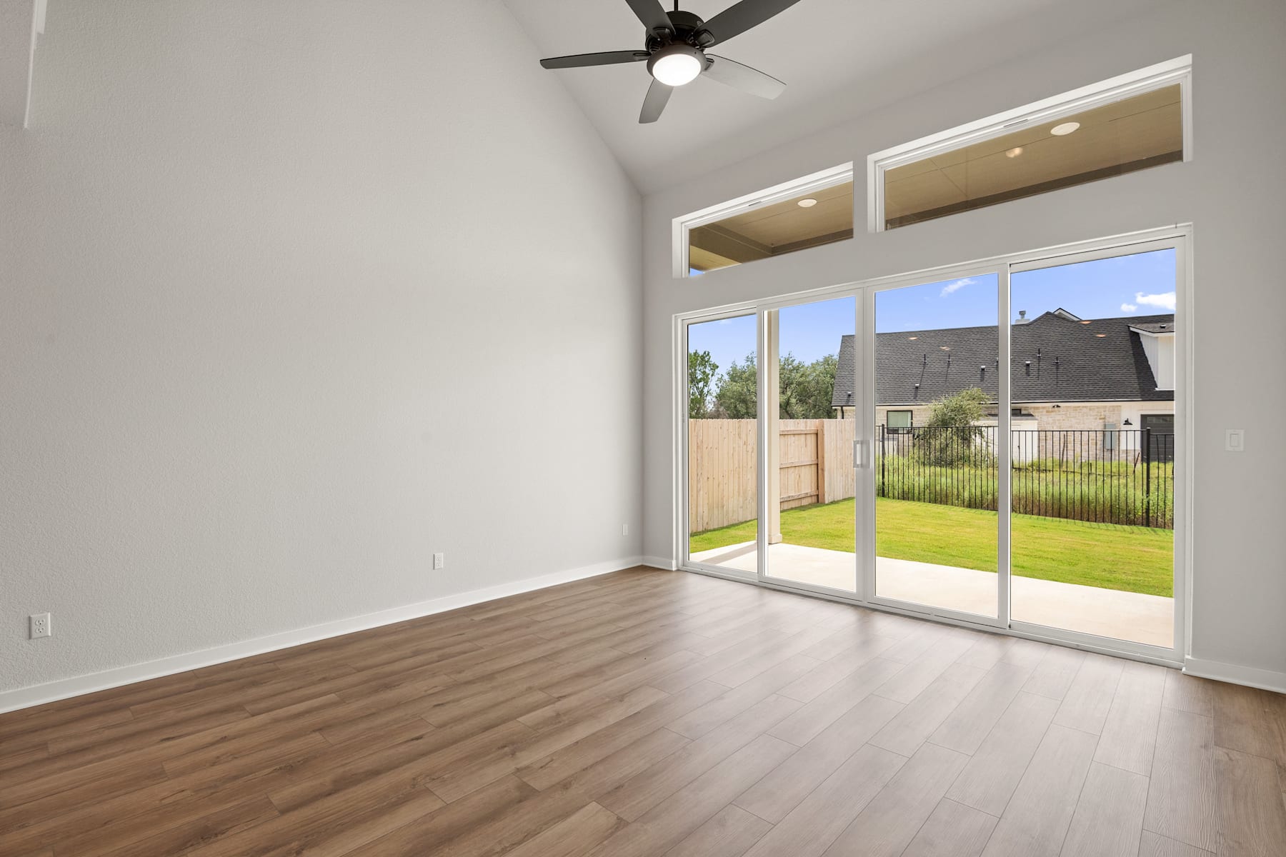 A spacious room with a sliding glass door leading to a grassy backyard, featuring a ceiling fan and hardwood flooring.