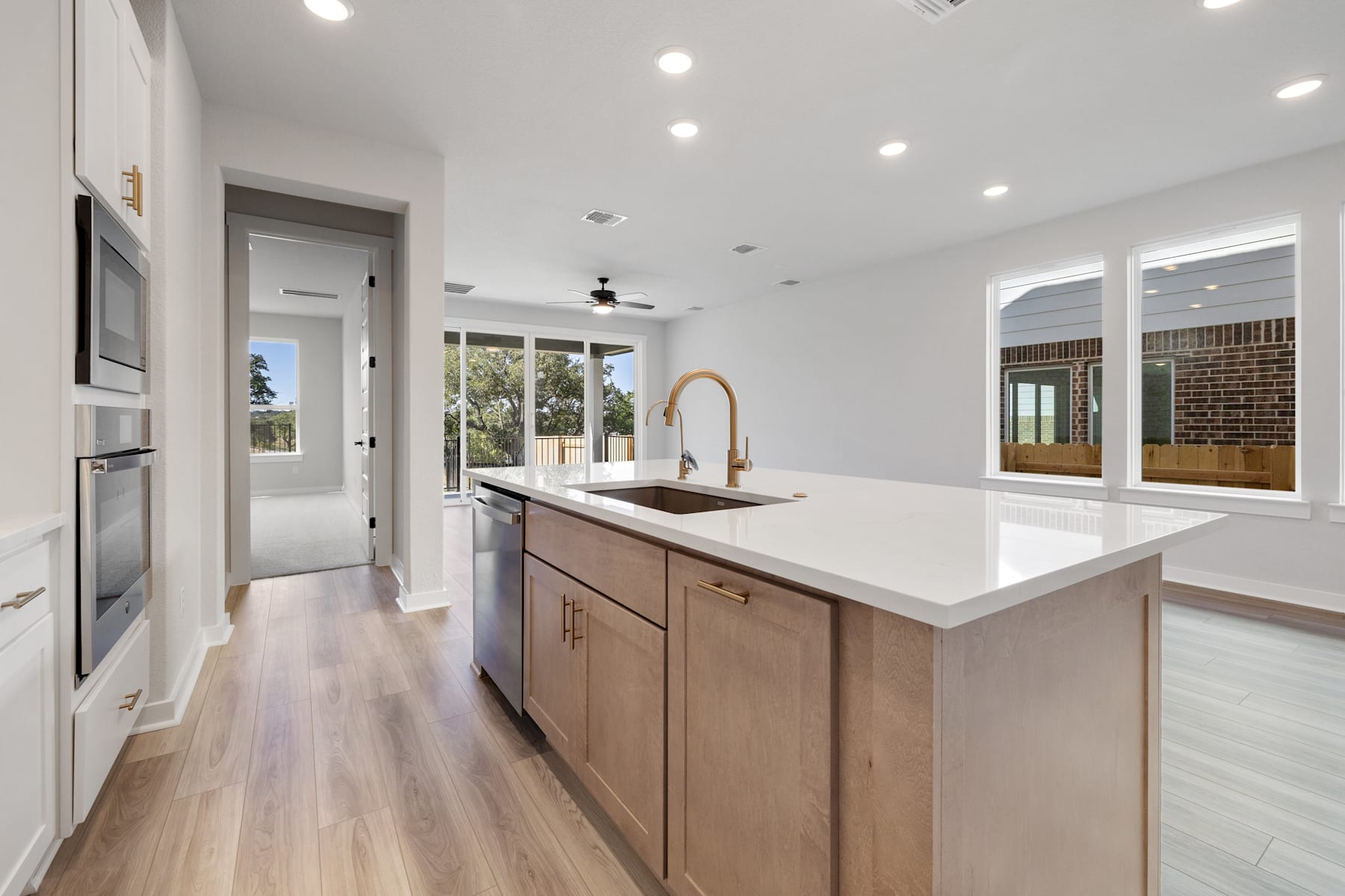 A modern, open-concept kitchen with light-colored wood cabinets, a white quartz countertop, and large windows providing ample natural light.