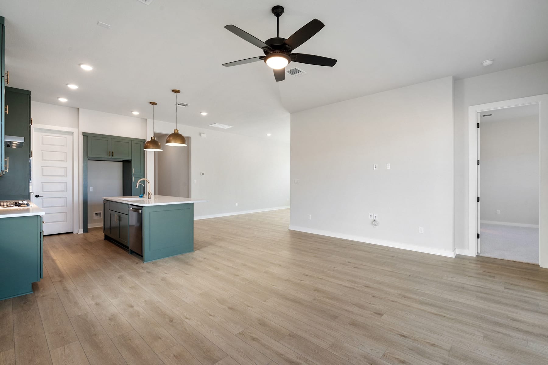 A modern, open-concept kitchen and living room with a ceiling fan, hardwood floors, and a green kitchen island.
