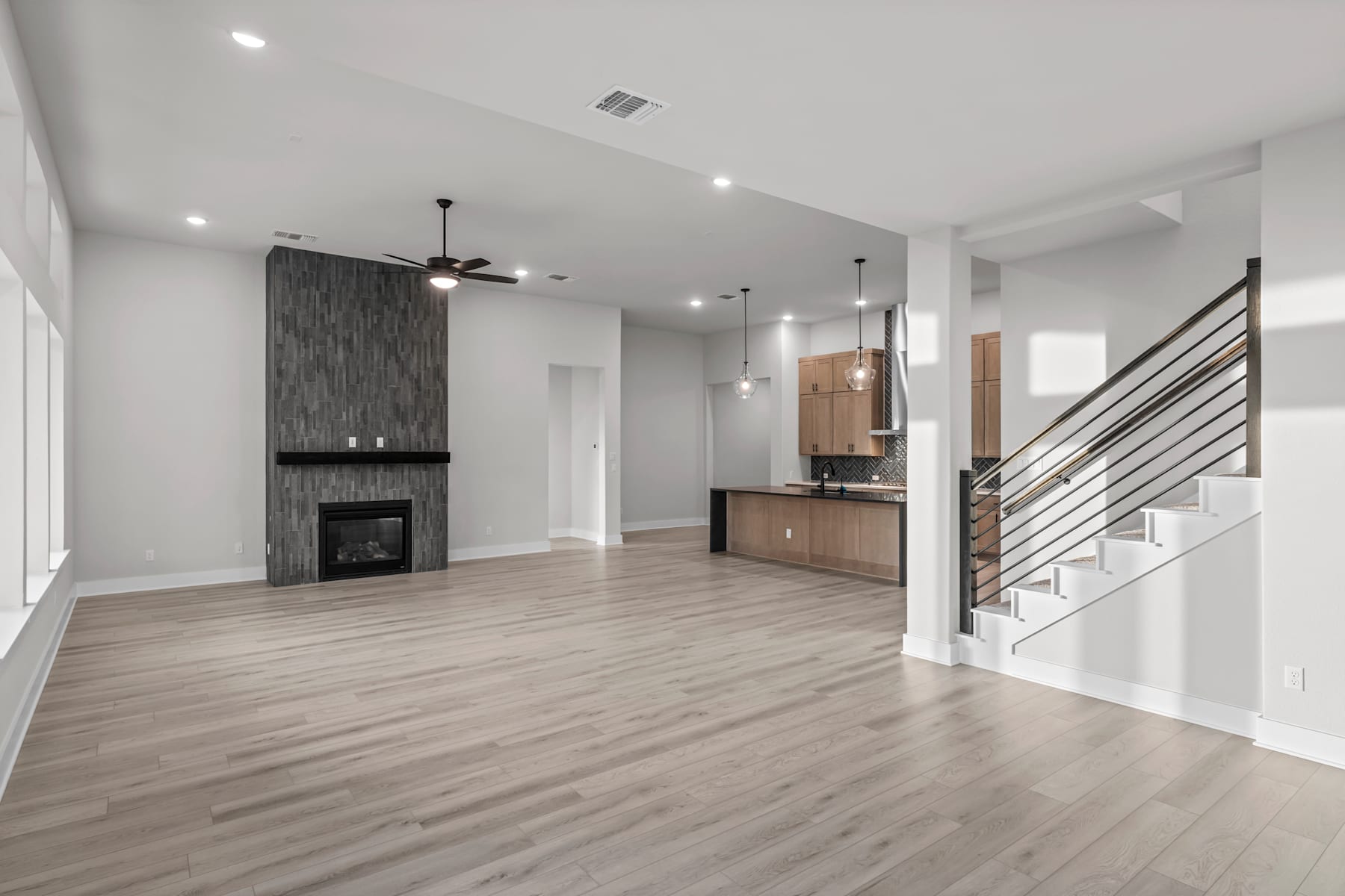 A modern, open-concept living space with a fireplace, hardwood floors, and a kitchen visible in the background.