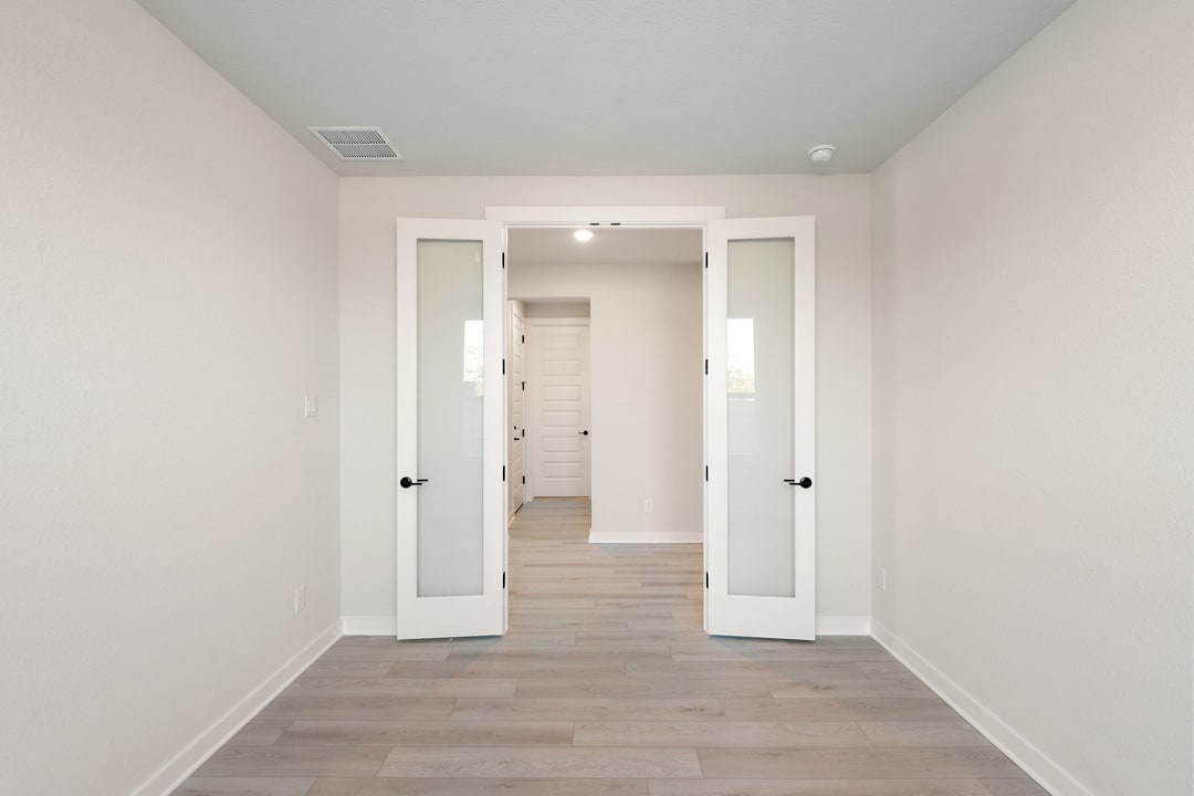 A bright, minimalist hallway with white walls, wooden flooring, and two white doors leading to other rooms.