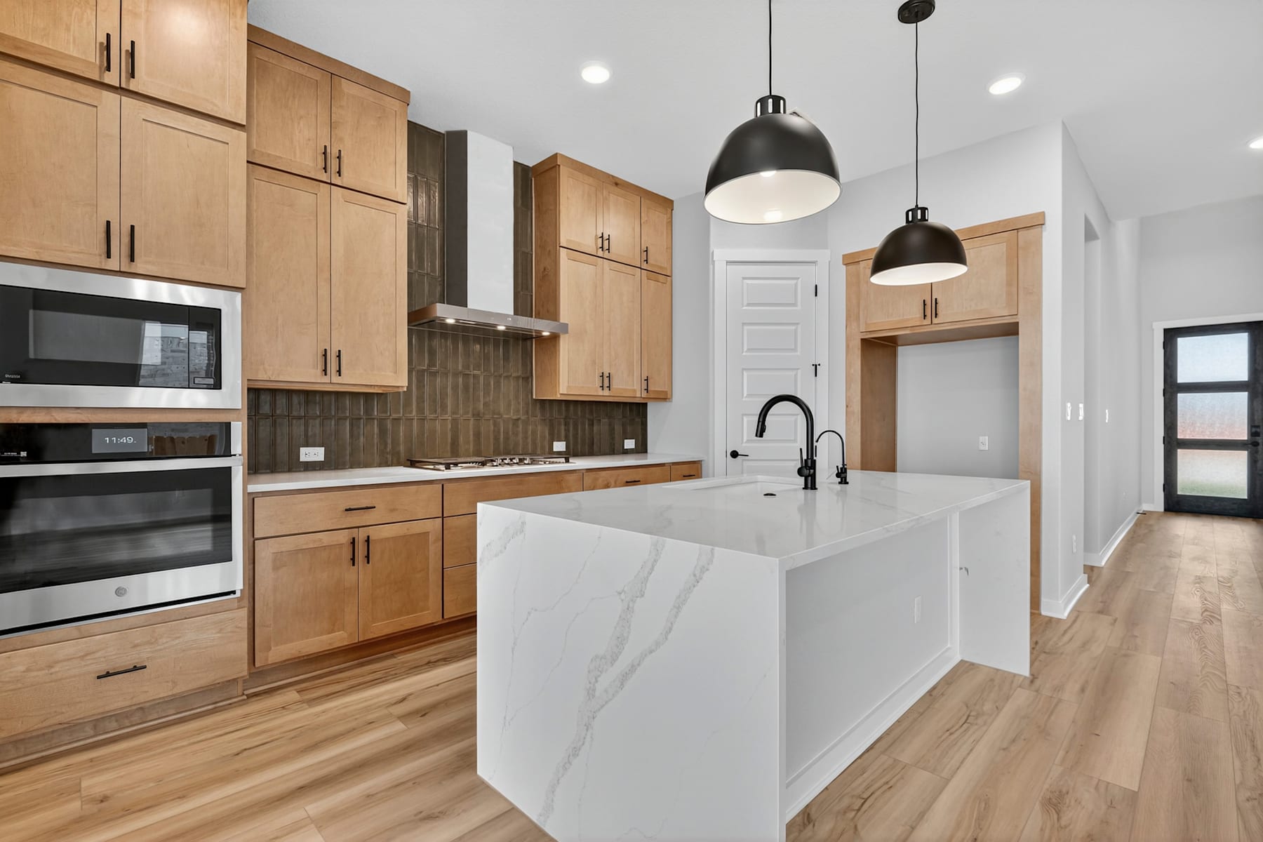 A modern and spacious kitchen with light wood cabinets, a white marble island, and pendant lights hanging above.