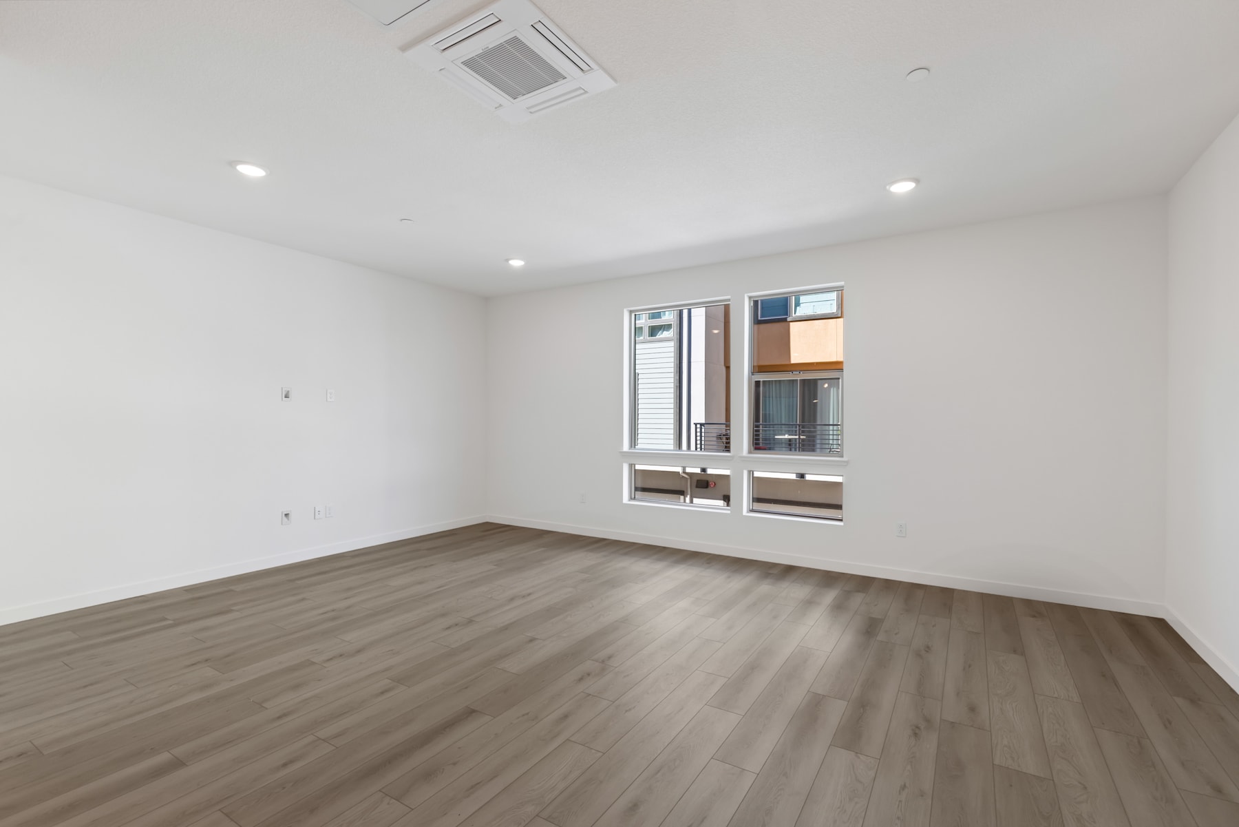 A spacious, well-lit room with a hardwood floor and a large window, providing a clean and minimalist interior design.